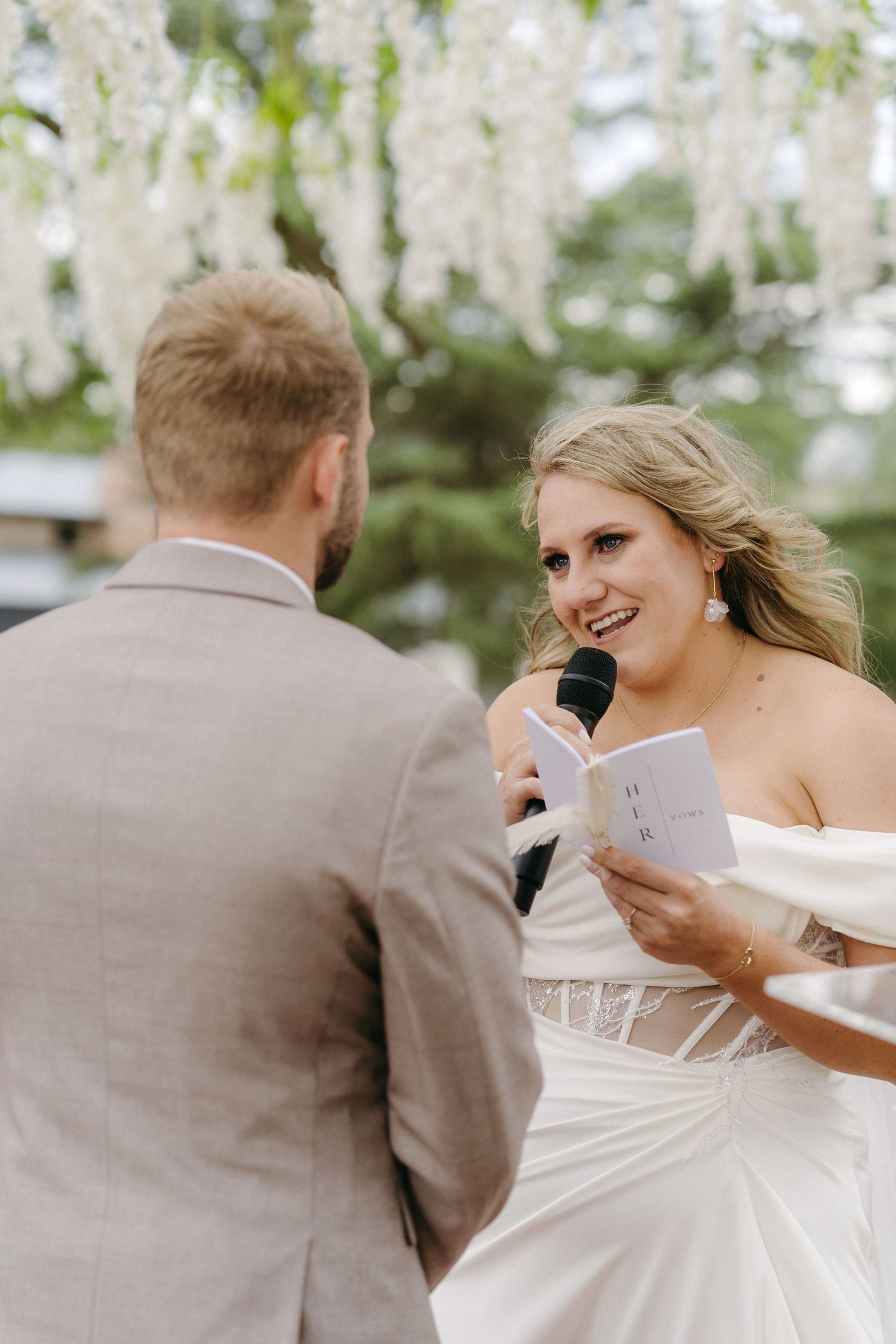 A couple exchanges vows during an outdoor wedding ceremony with white blossoms in the background.