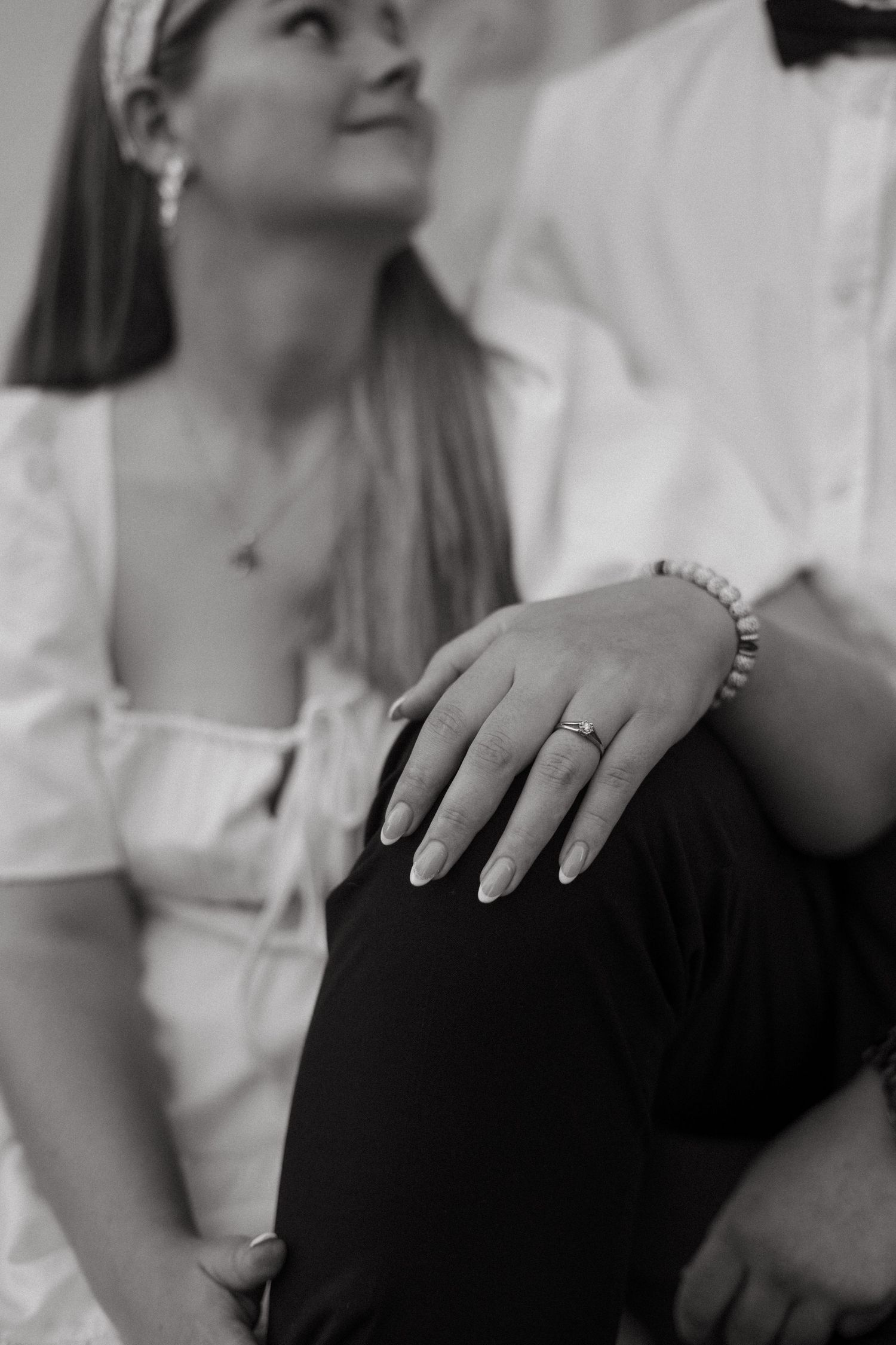 Black and white photo showing a hand with an engagement ring and bracelet resting against dark pants.