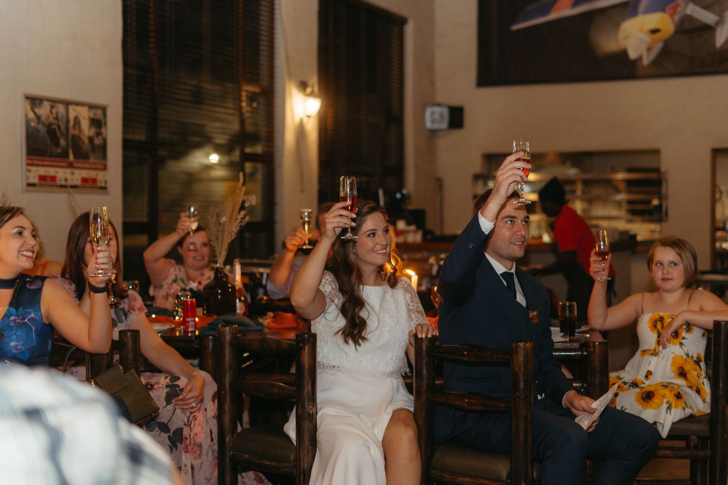 Wedding celebration with guests raising glasses for a toast under string lights.