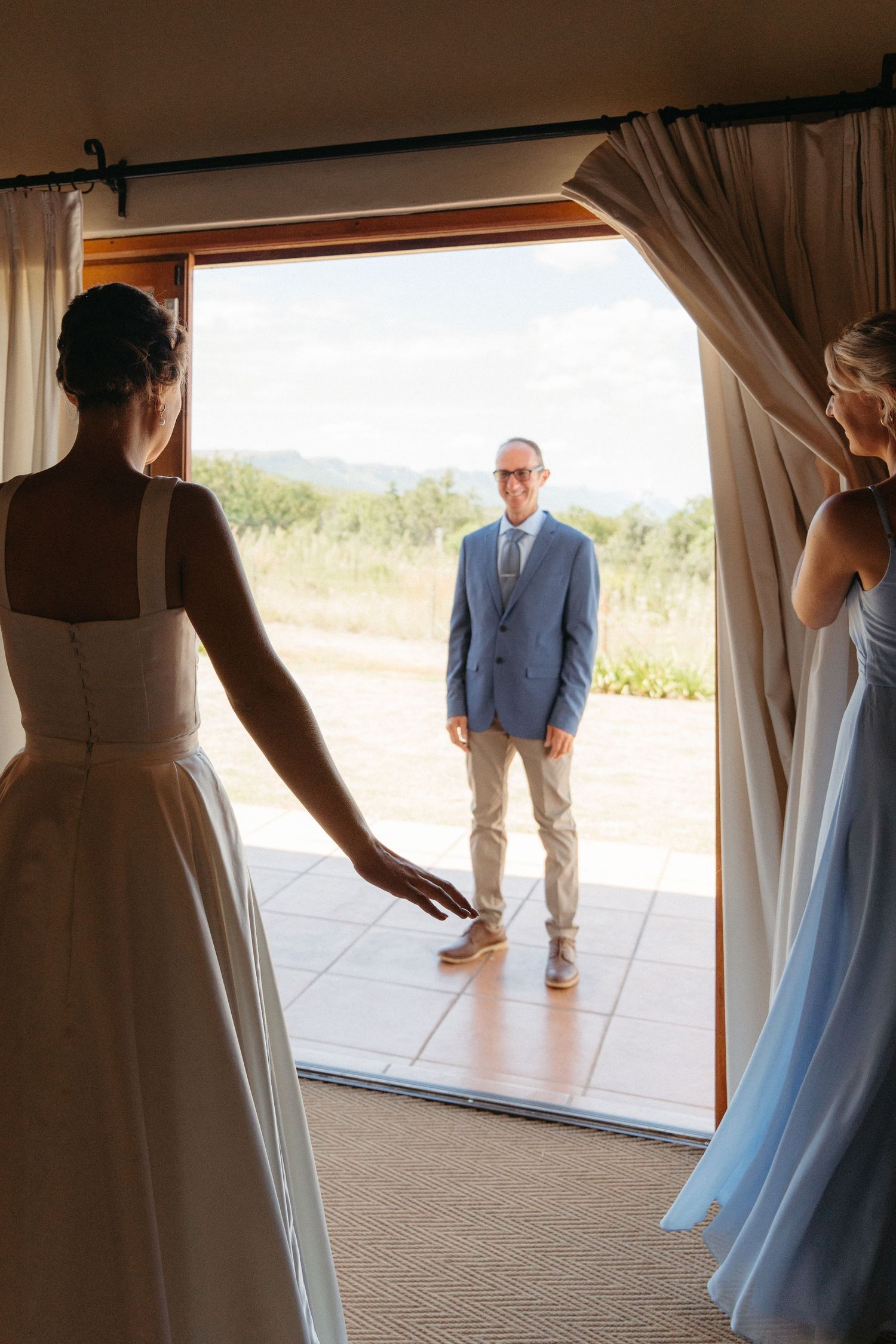 A series of candid wedding photos showing a first look moment through glass doors at an outdoor venue.