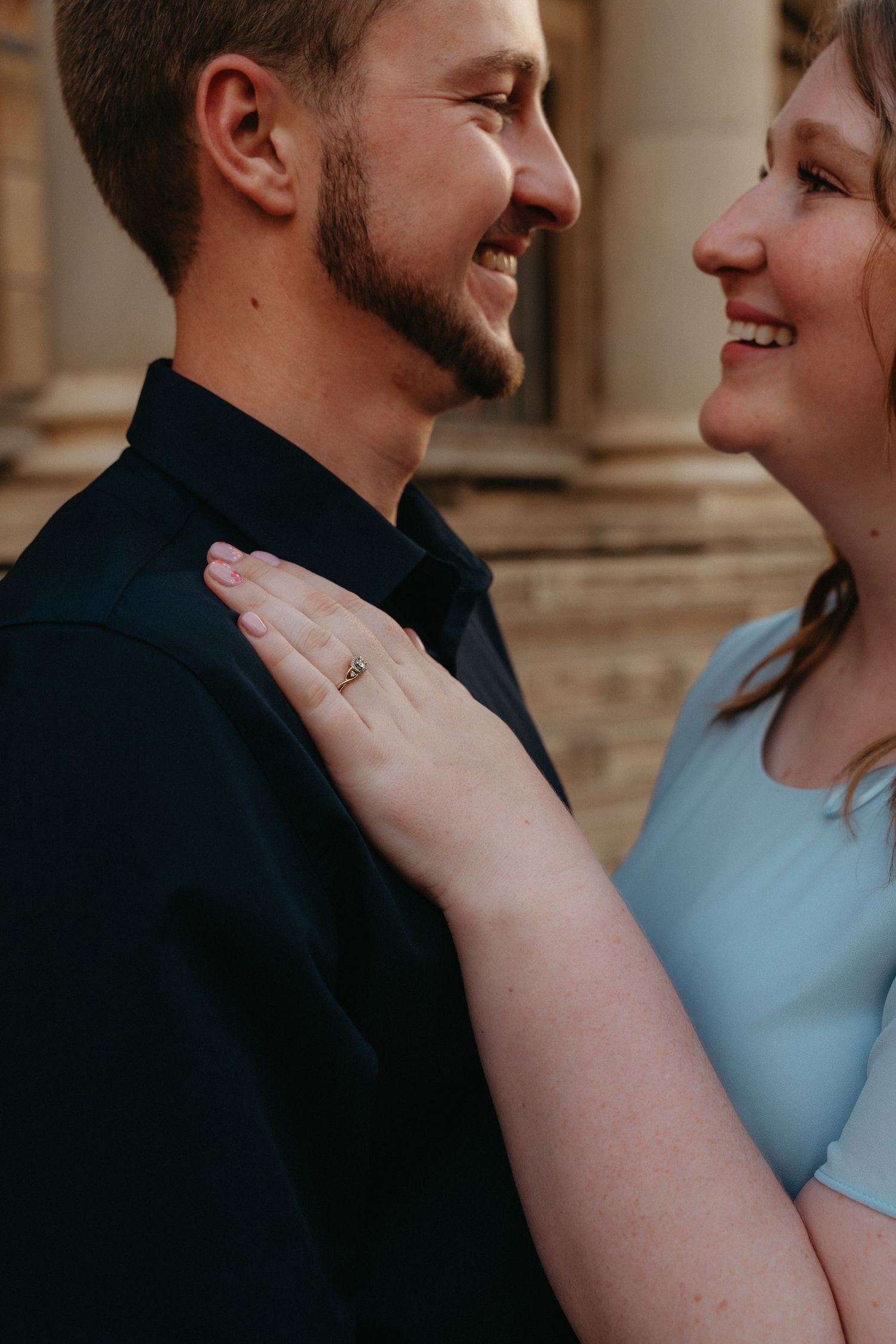 A couple shares a tender moment together as they smile at each other while the woman rests her hand on his chest.