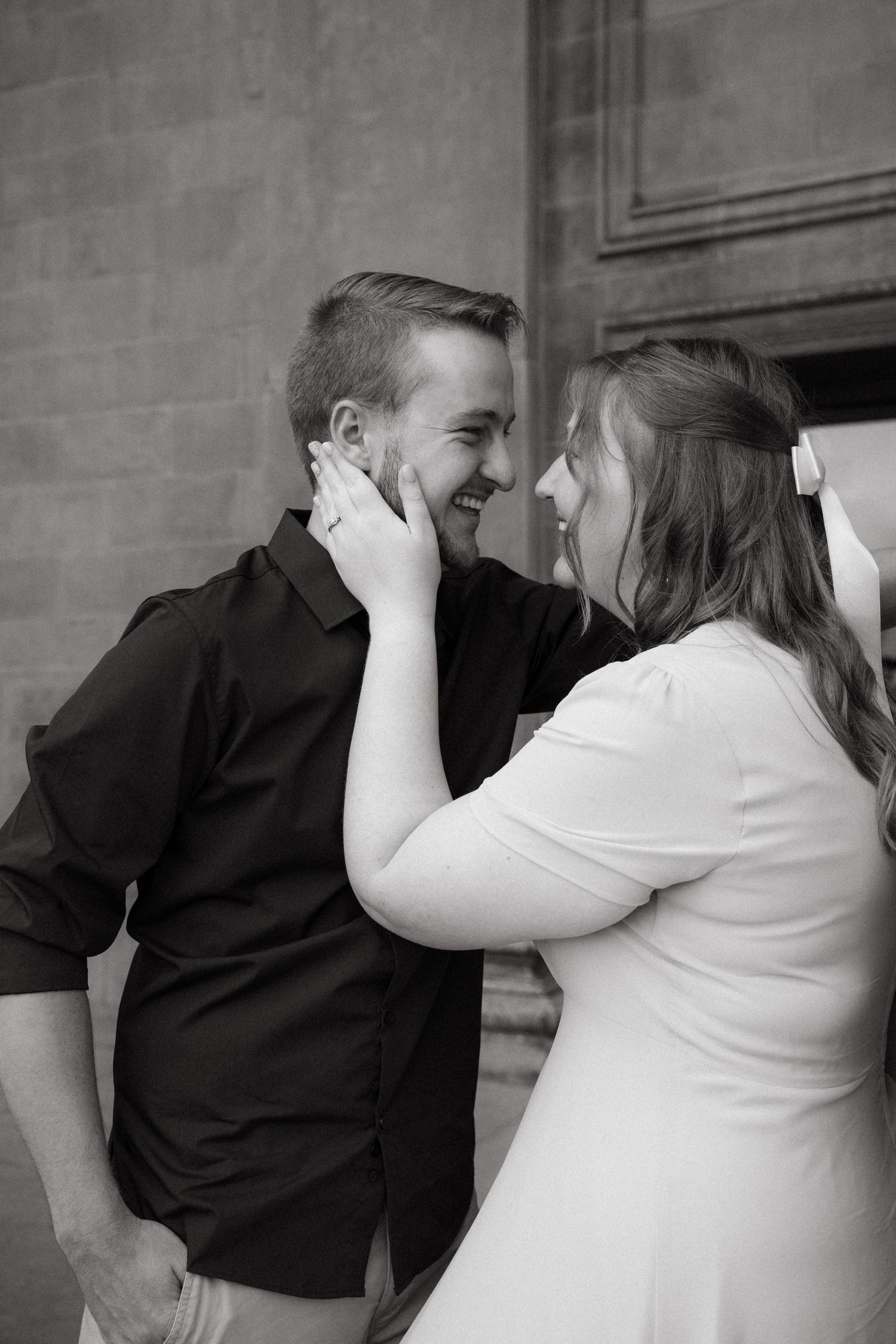 A tender black and white romantic moment between a couple as they share an intimate gesture against a brick wall.