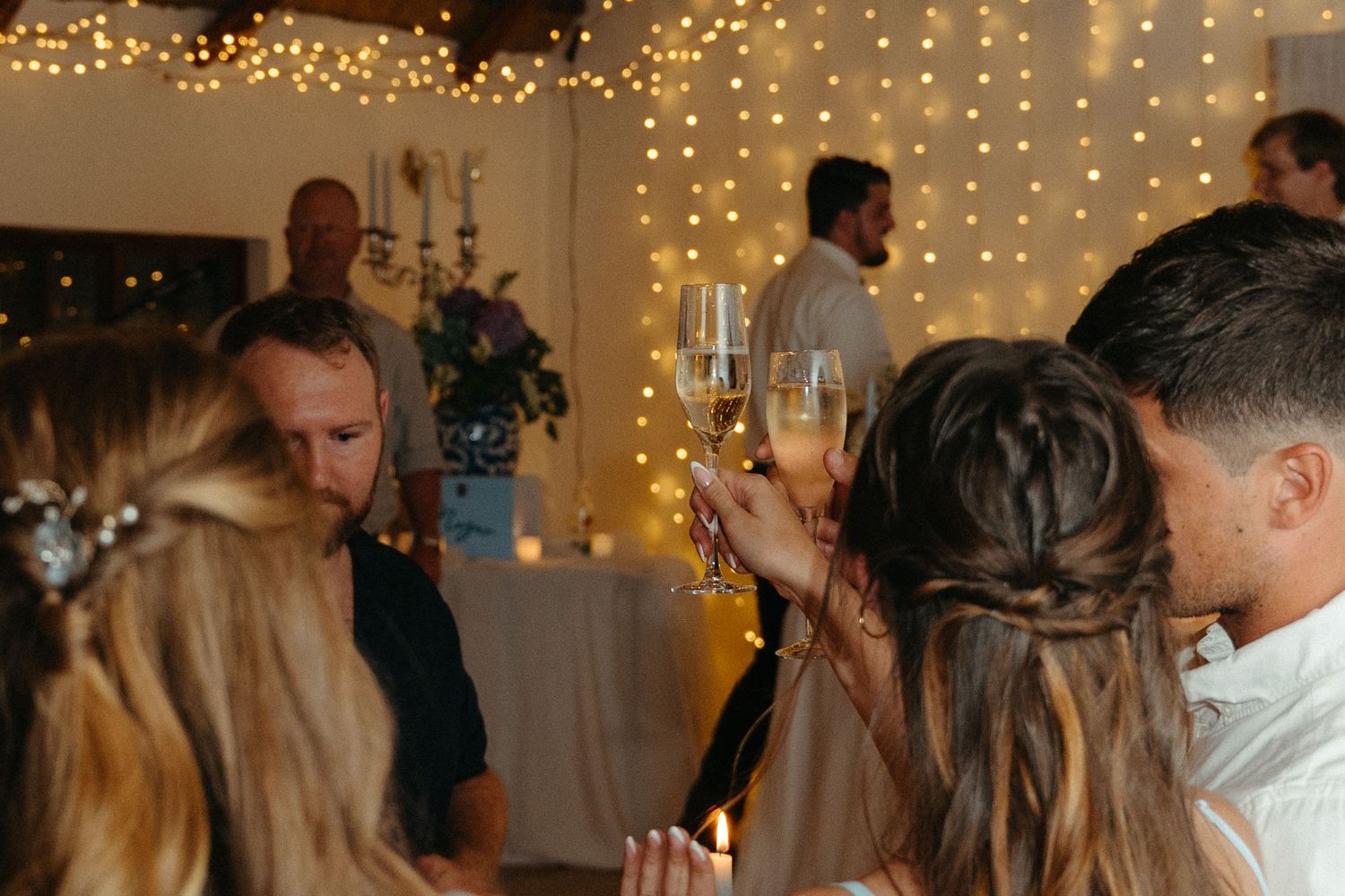 Wedding guests dance and celebrate on a dimly lit dance floor decorated with twinkling string lights.