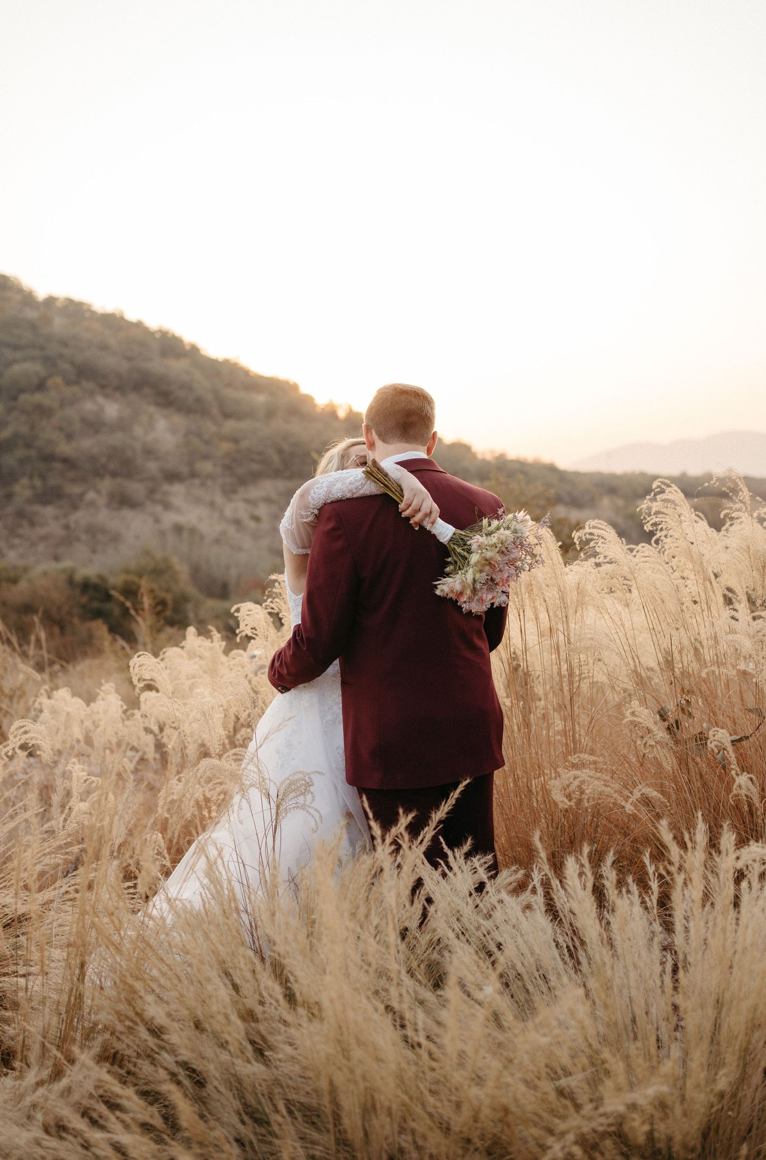 A couple embraces in a field of golden pampas grass during a winter sunset with mountains in the background.