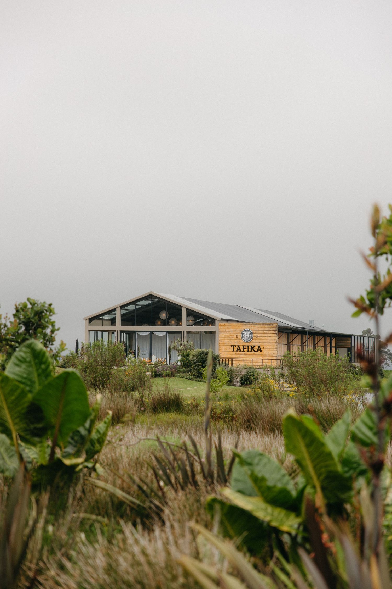 Tafika building surrounded by lush greenery and wild grasses under an overcast sky in a natural landscape setting.