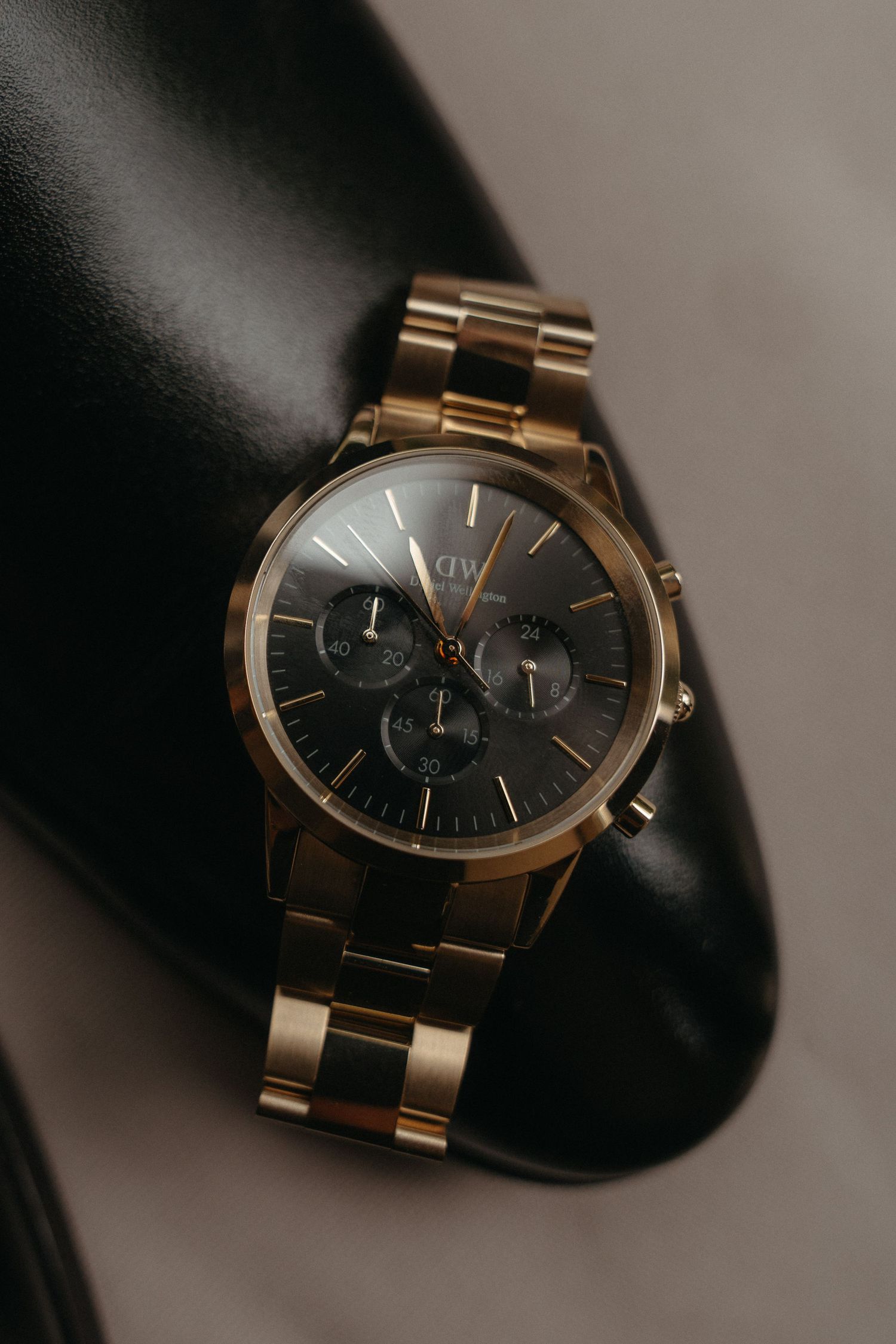 Daniel Wellington rose gold chronograph watch with black dial resting on a dark leather shoe.