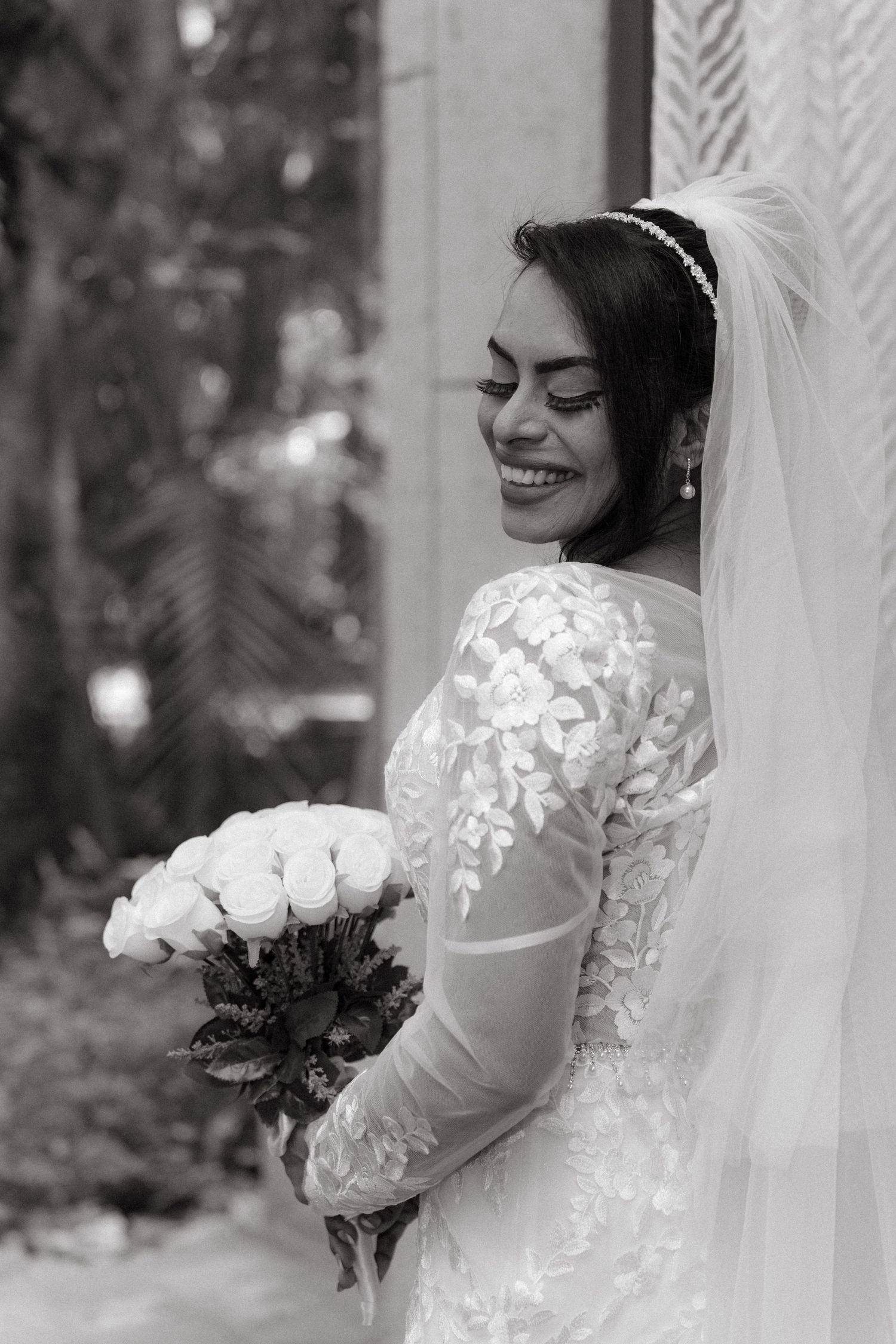 Black and white portrait of smiling bride in lace gown holding white rose bouquet at The Palace at Sun City