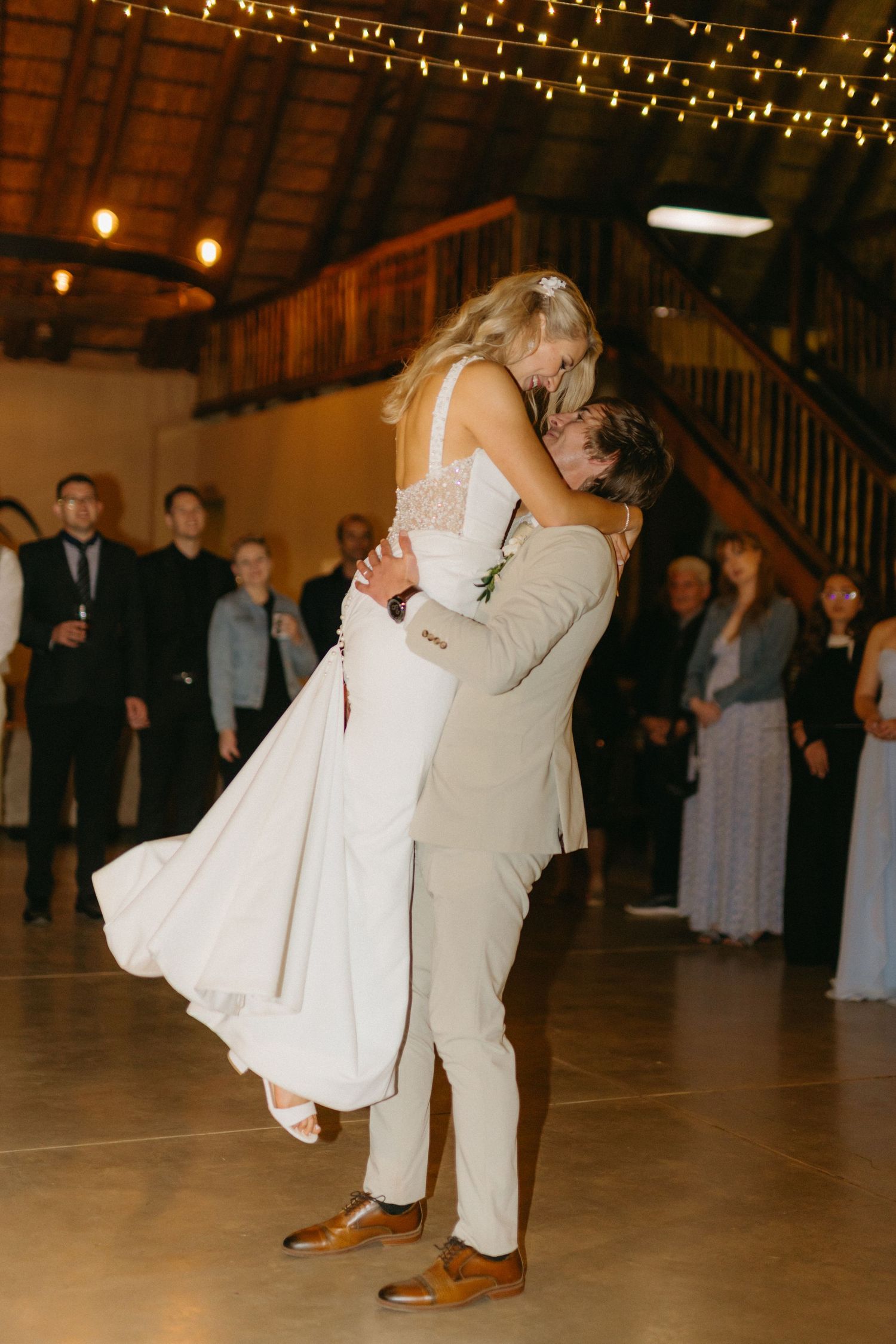 Couple dancing in a rustic venue decorated with string lights overhead.