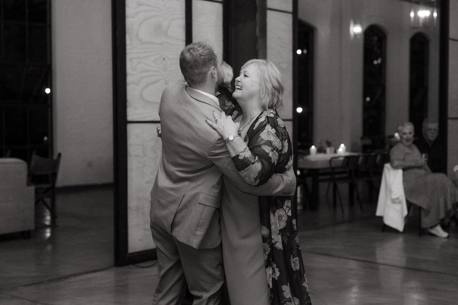 A couple shares a romantic dance together in a dimly lit reception venue, captured in black and white.