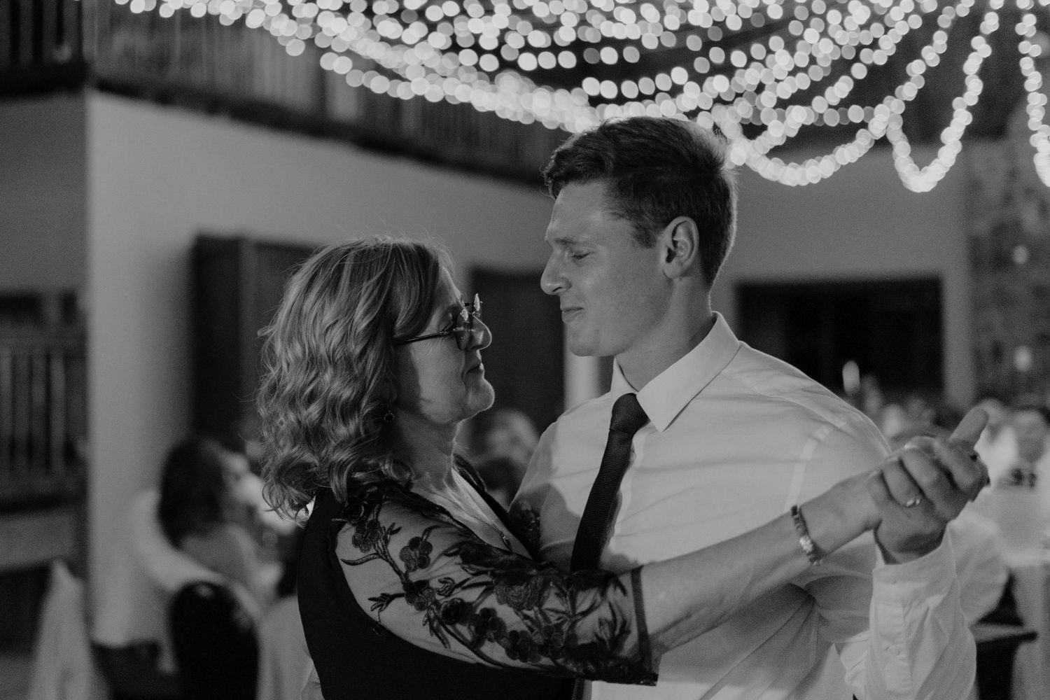 Couples dancing together under twinkling lights at an evening wedding celebration.