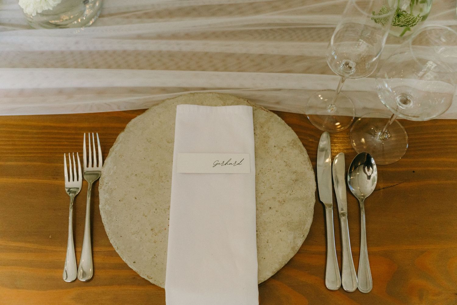 Elegant table setting with white plate, silver cutlery, and napkin on wooden surface.