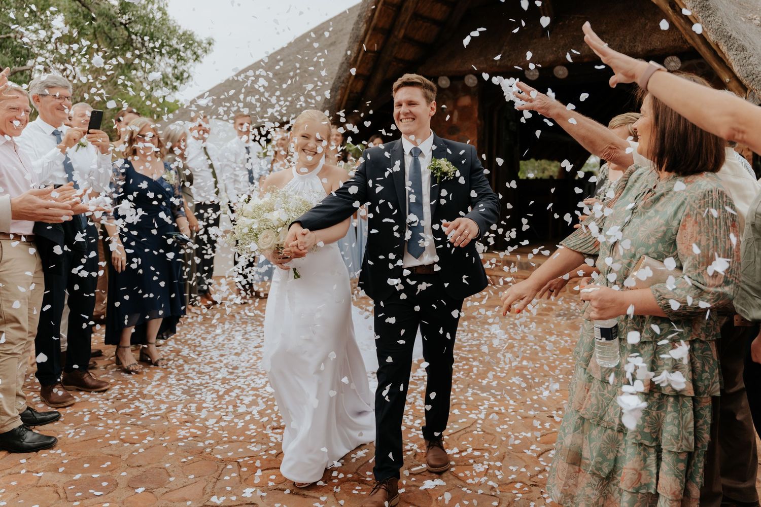 Wedding guests shower newlyweds with confetti during celebratory recessional walk outdoors.