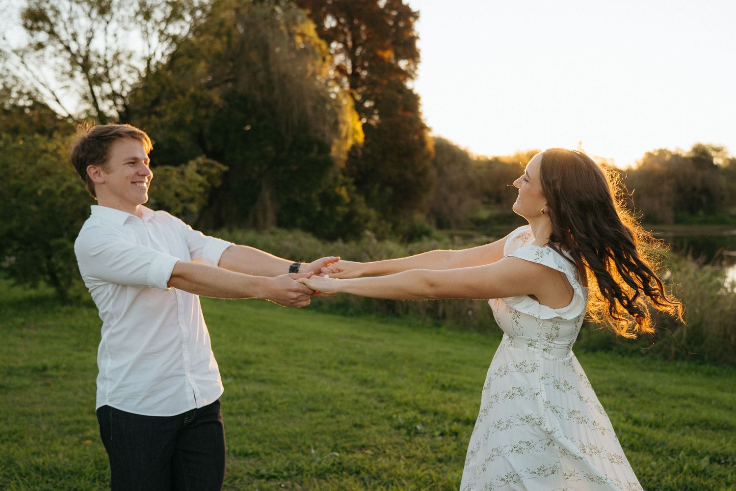 A couple dances together on a grassy field at sunset, spinning and holding hands in romantic summer lighting.