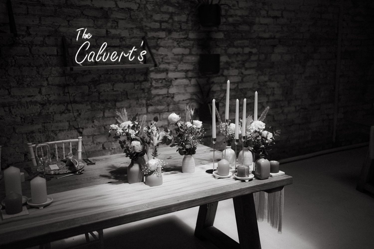 Elegant wedding reception table setup with candles and floral arrangements against a brick wall backdrop.