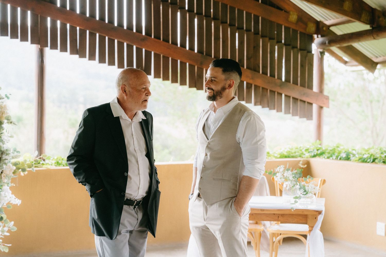 Wedding party members gather under covered outdoor patio area.