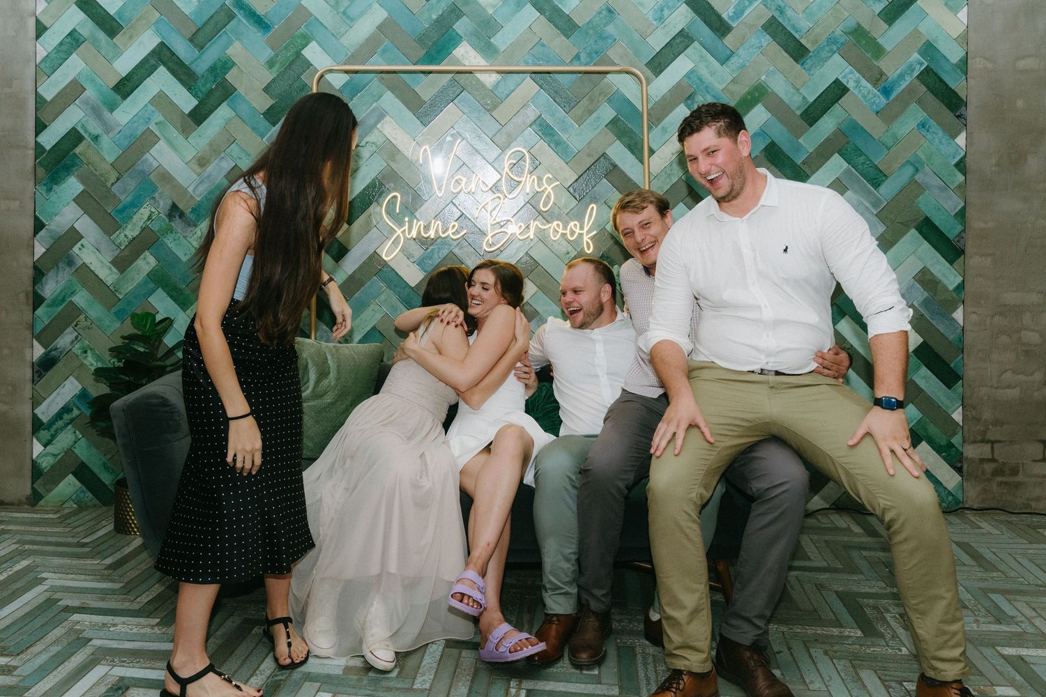 A family poses together against a teal chevron backdrop with a decorative neon sign during a photo session.