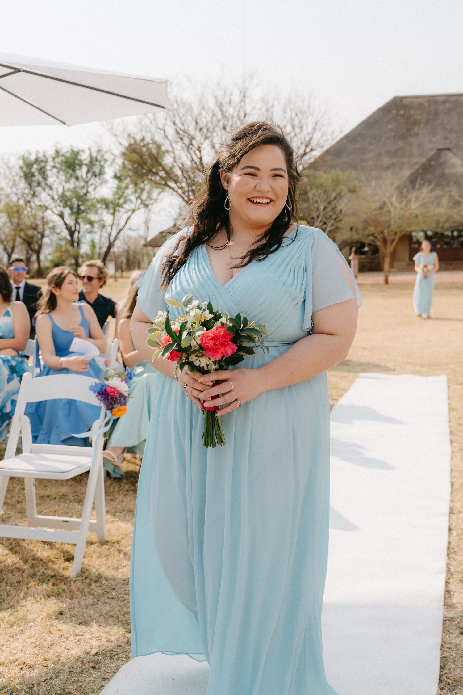 Bridesmaids in light blue dresses hold vibrant bouquets at an outdoor desert wedding venue.