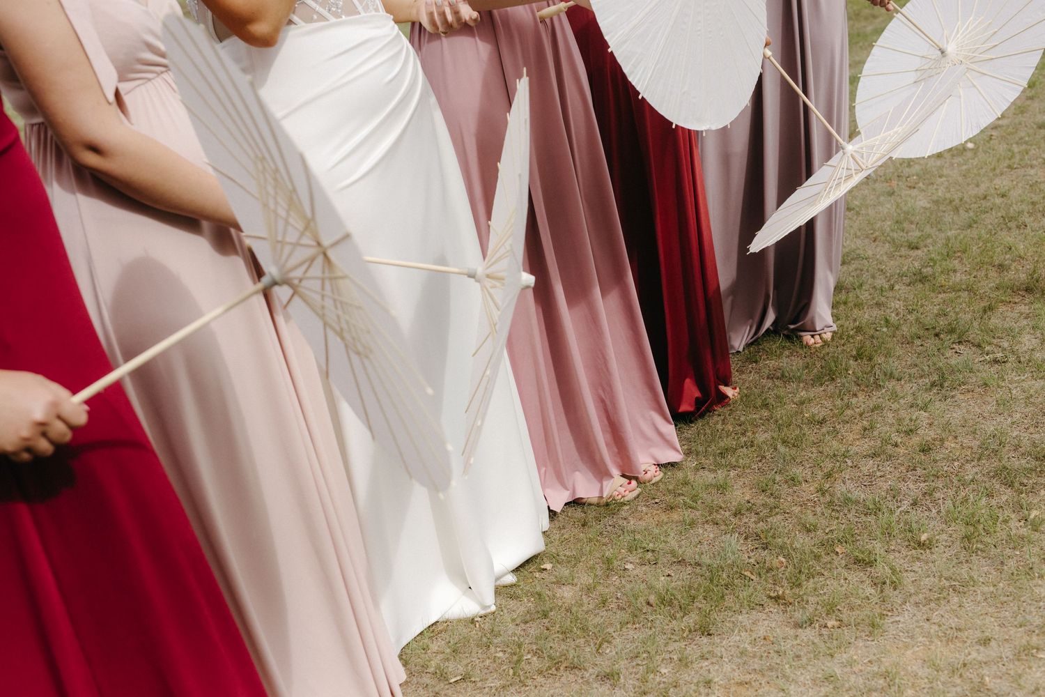 Row of flowing dresses in white and pink shades against grass with paper fans creating an elegant outdoor scene.