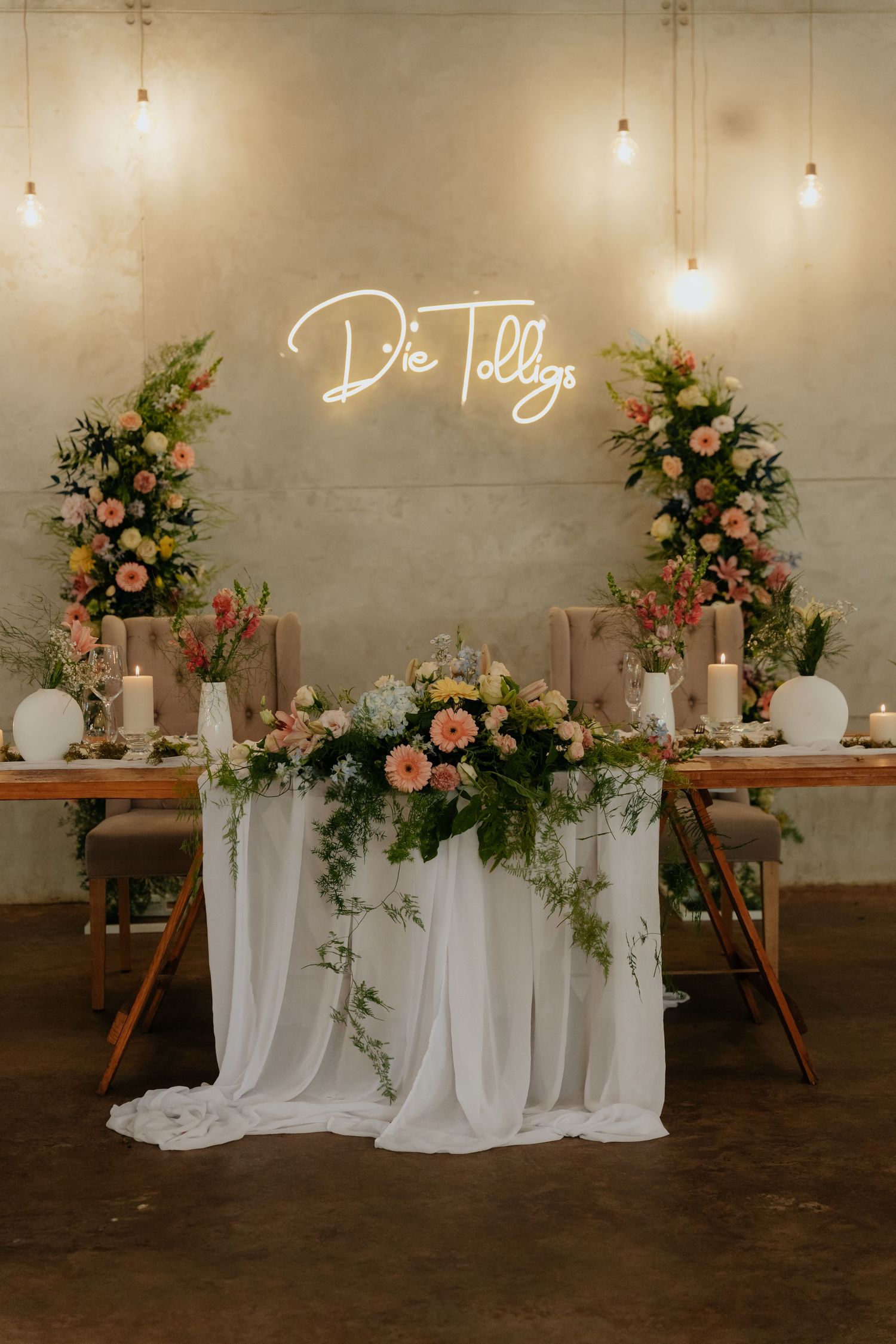 Sweetheart table with neon sign, floral arrangements, candles, and hanging Edison bulbs in @Boshoek Venue in Lydenburg, South Africa