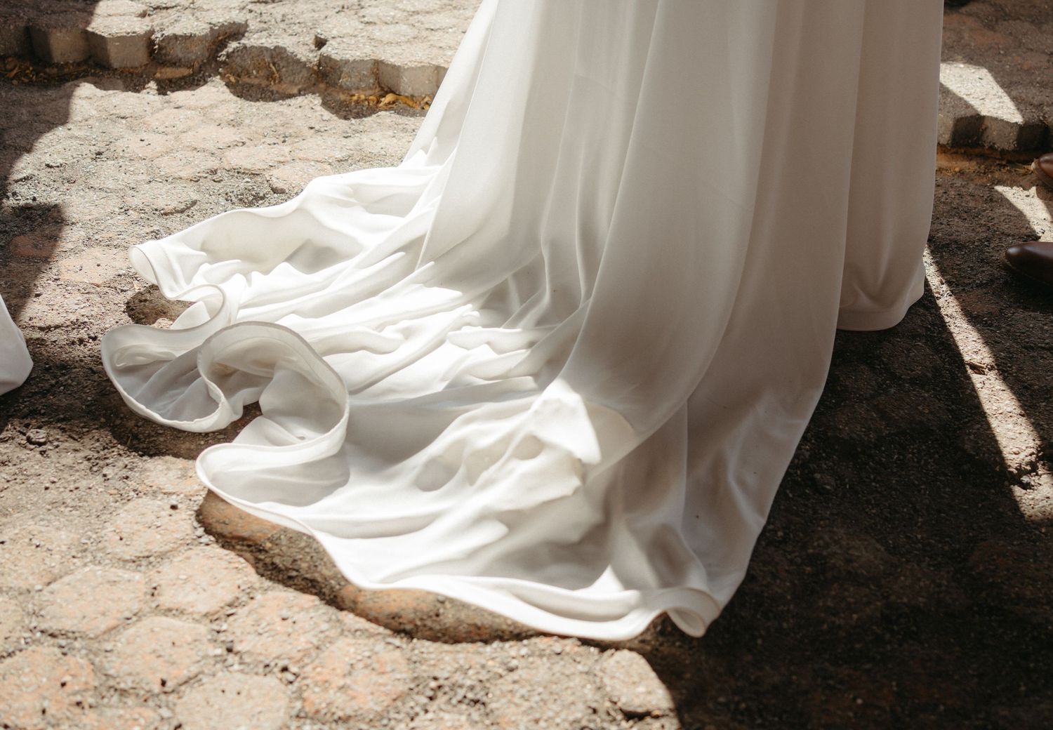 Close-up of a flowing white wedding dress train against stone pavement.