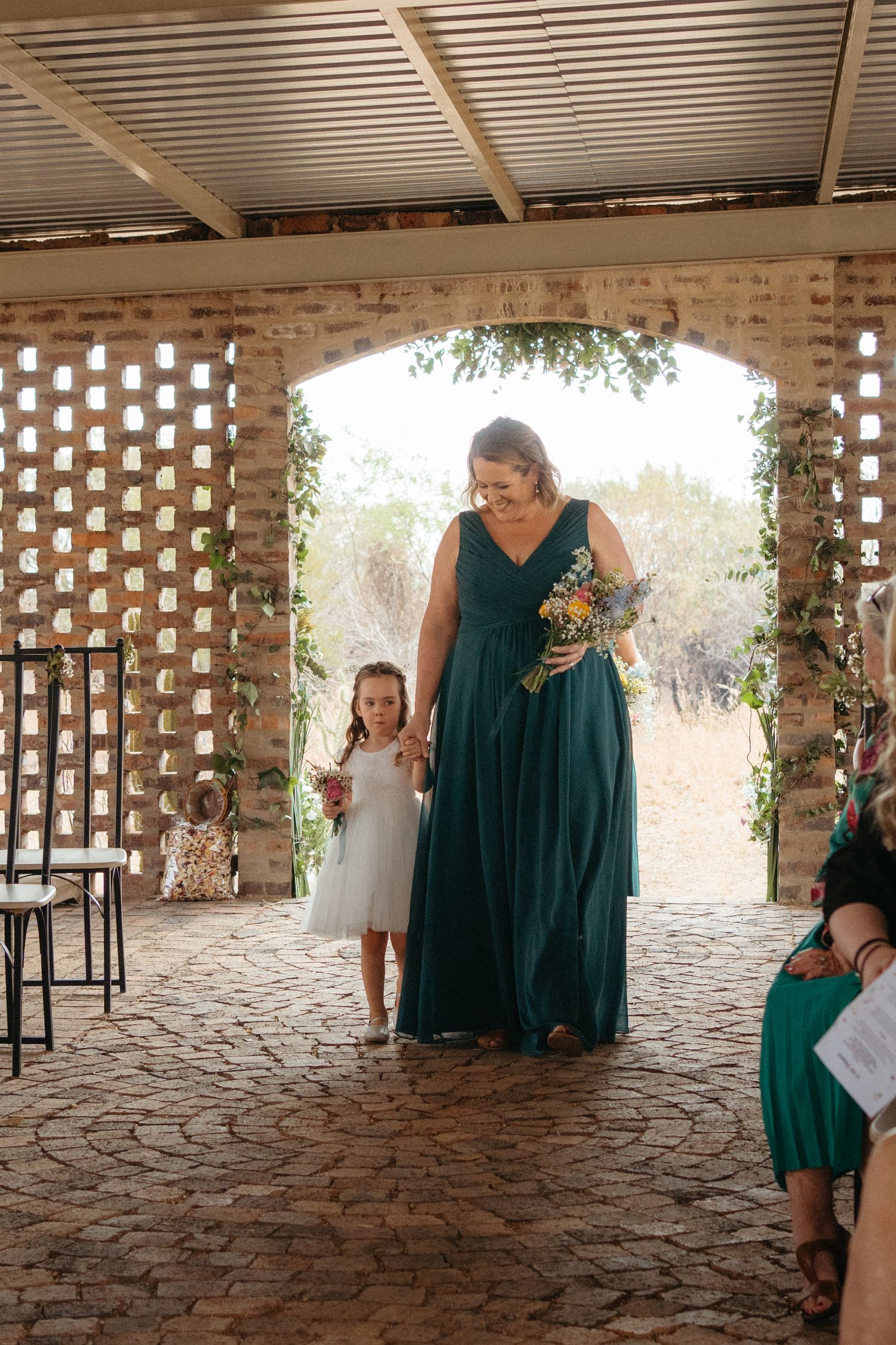 A formal wedding procession under a brick archway with decorative lattice walls.