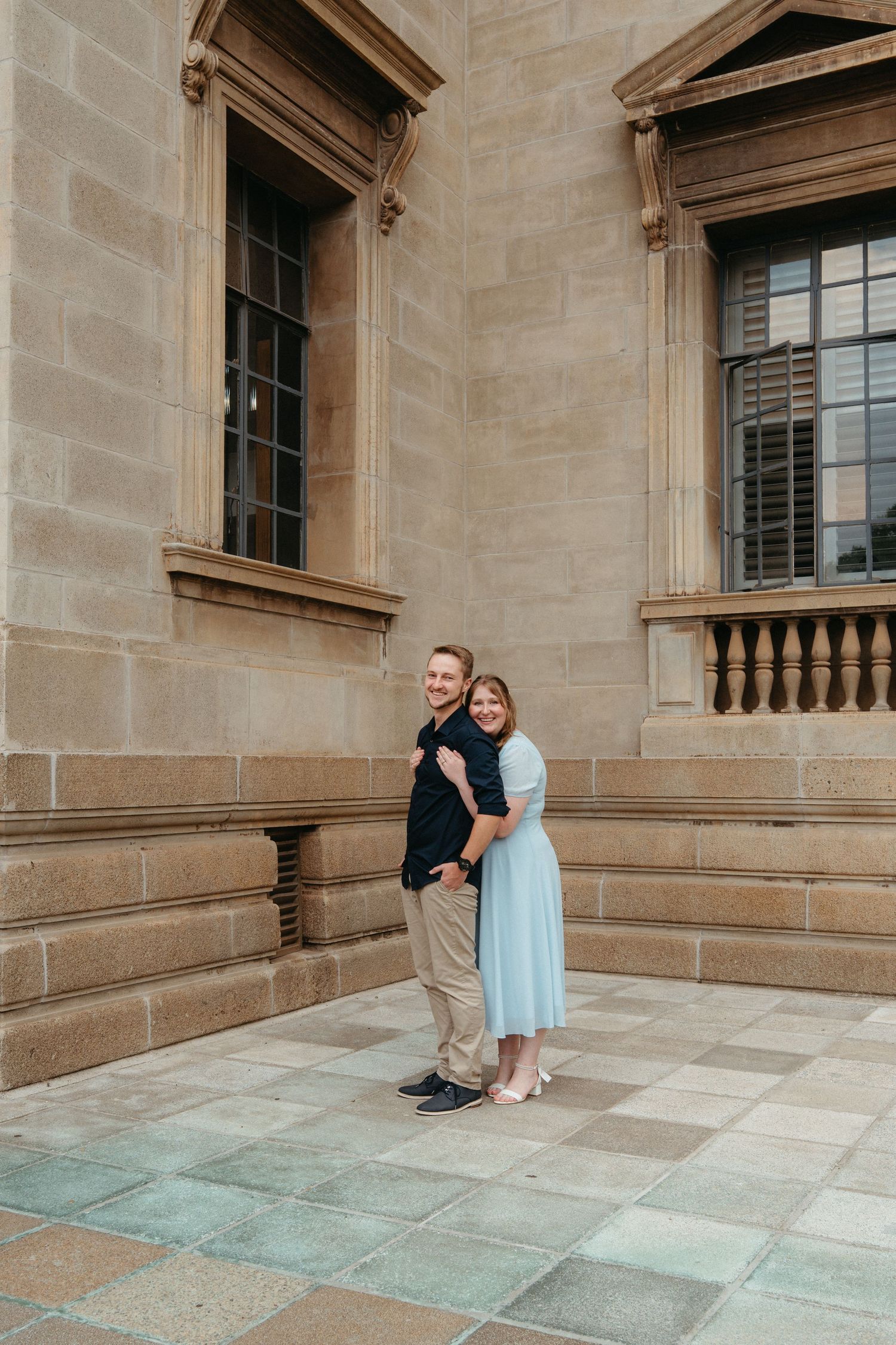 A couple poses together in a series of photos against a stone building's architectural backdrop with arched windows.