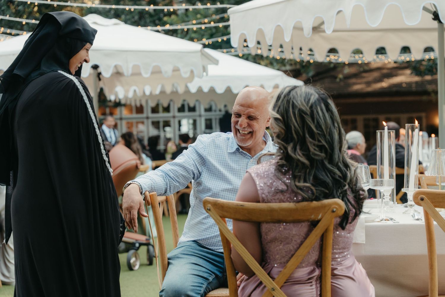 Guests laughing and enjoying conversation at an outdoor wedding reception under white tent canopies.
