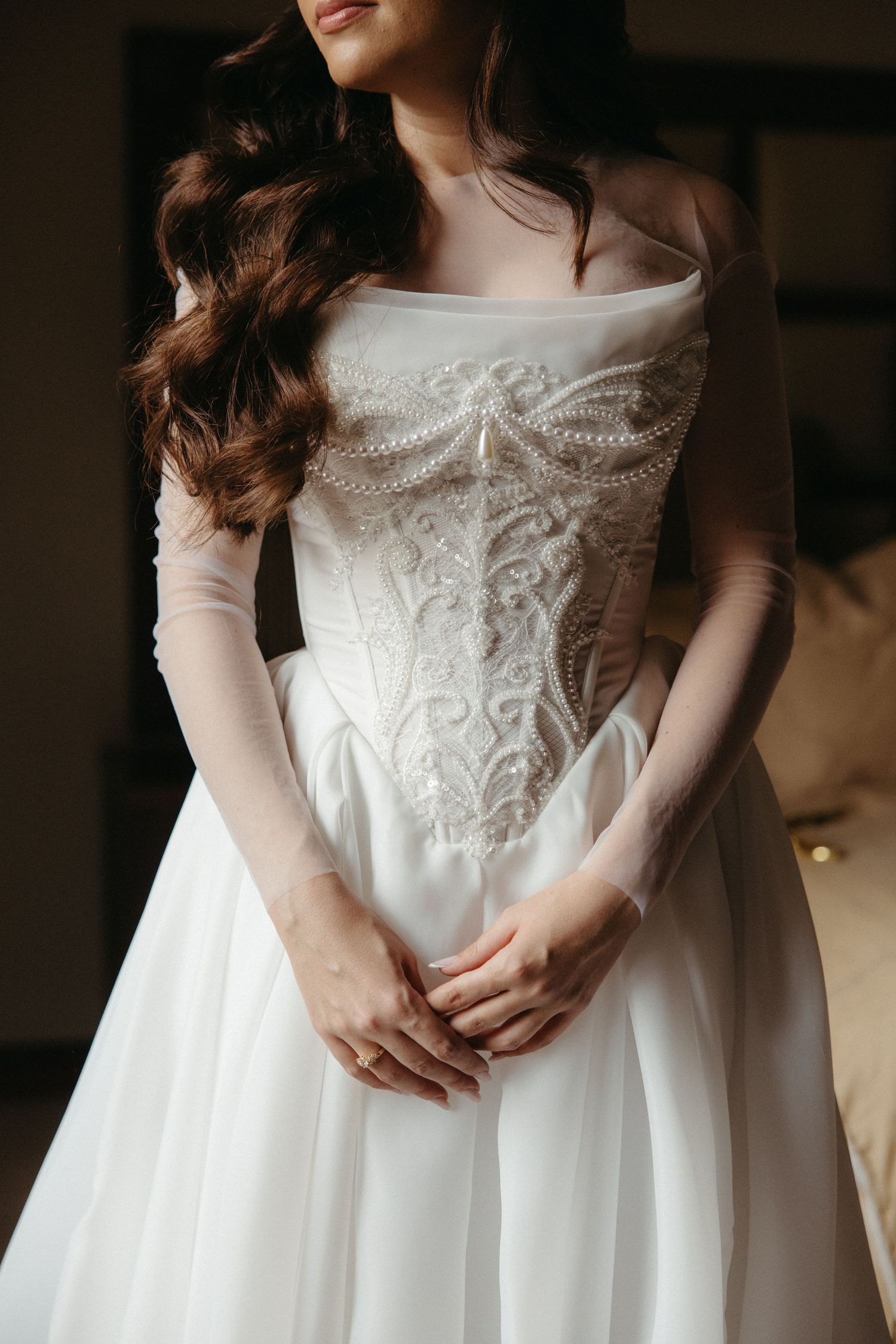 Bride in an elegant beaded corset wedding gown with sheer sleeves clasps her hands at her Johannesburg wedding.