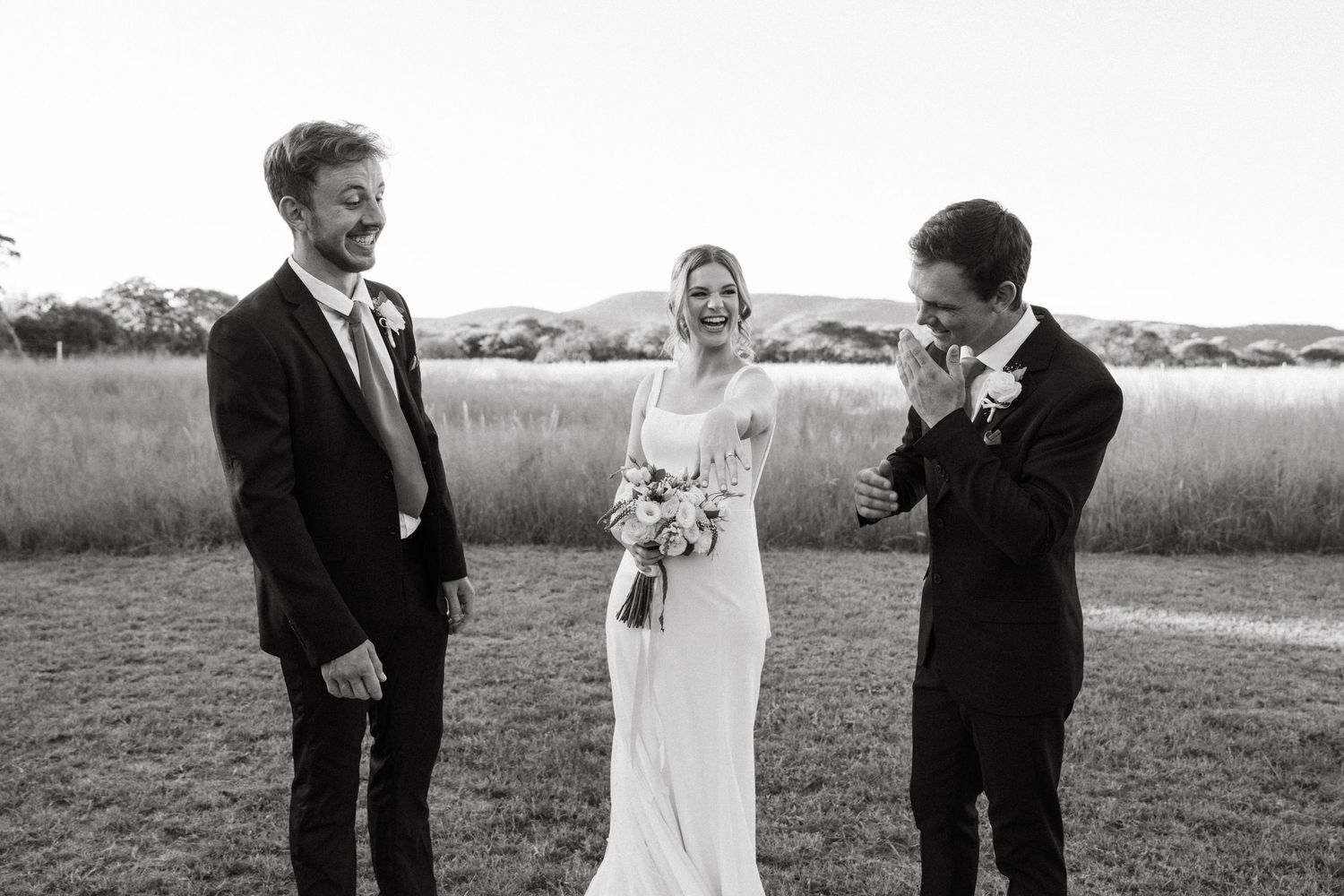 Black and white wedding photo with group sharing joyful moment together in outdoor field setting.