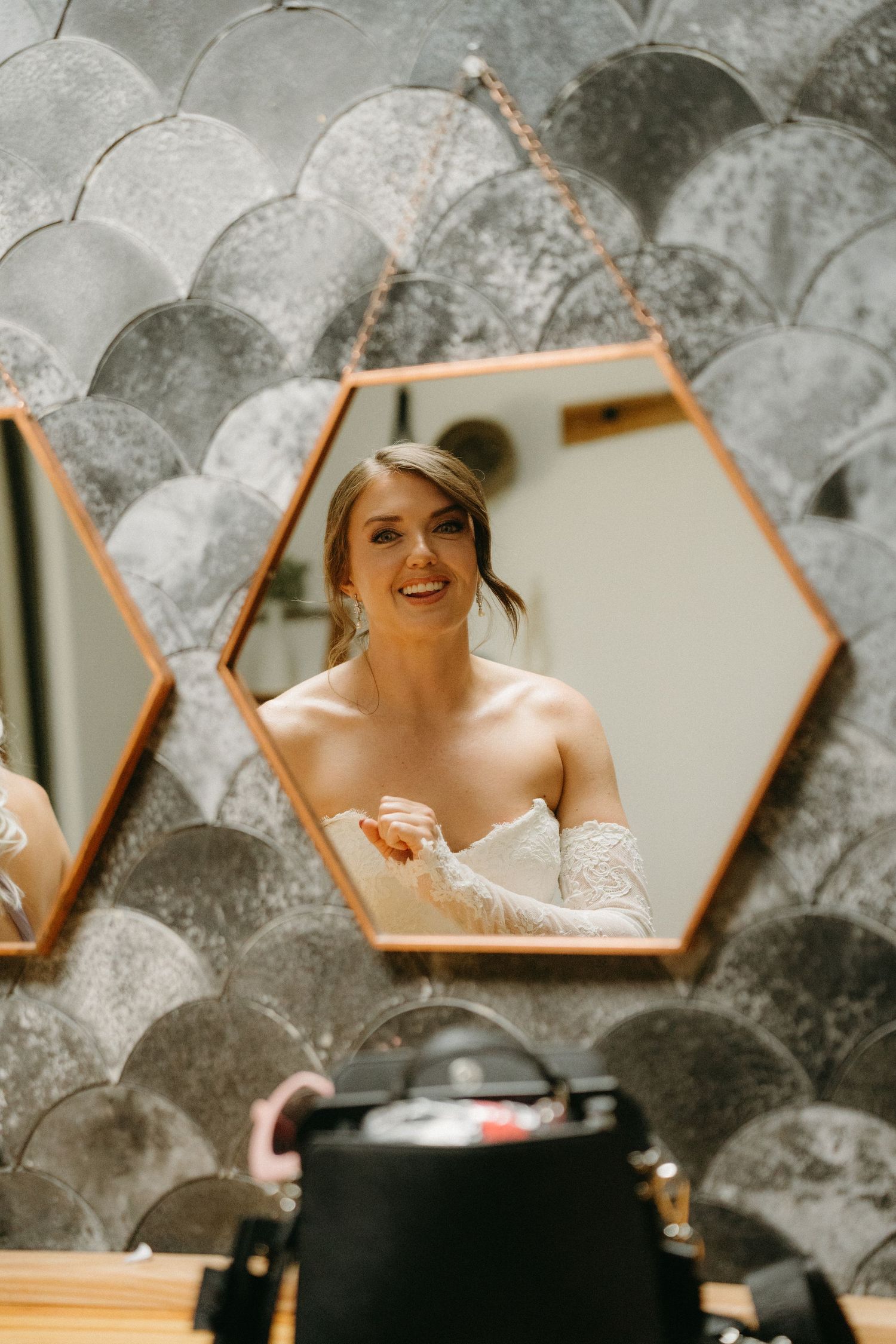 A hexagonal mirror reflection shows a bride getting ready with a scalloped wall pattern in the background.