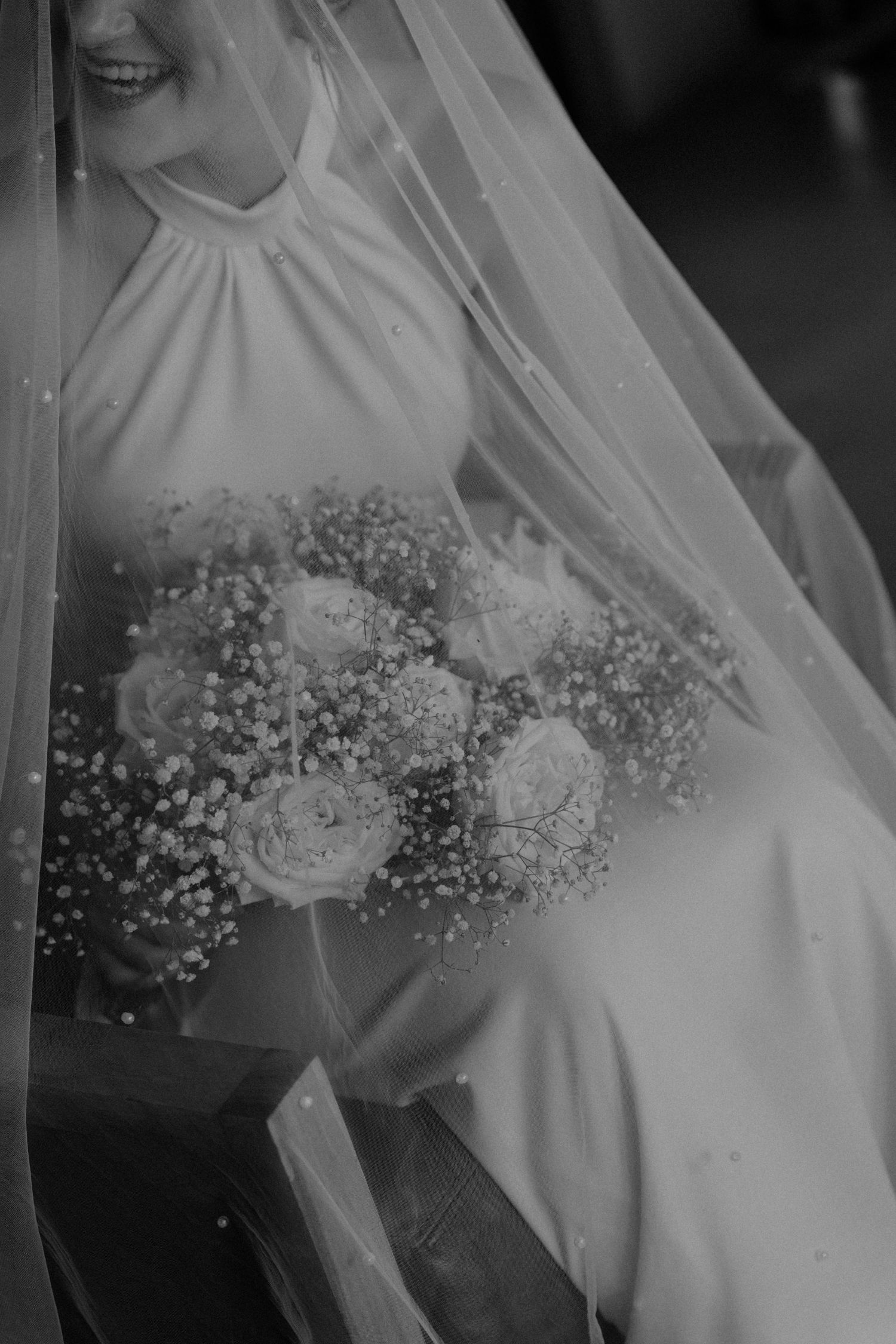A bride in a white dress holds a delicate bouquet of baby's breath flowers against a dark background.