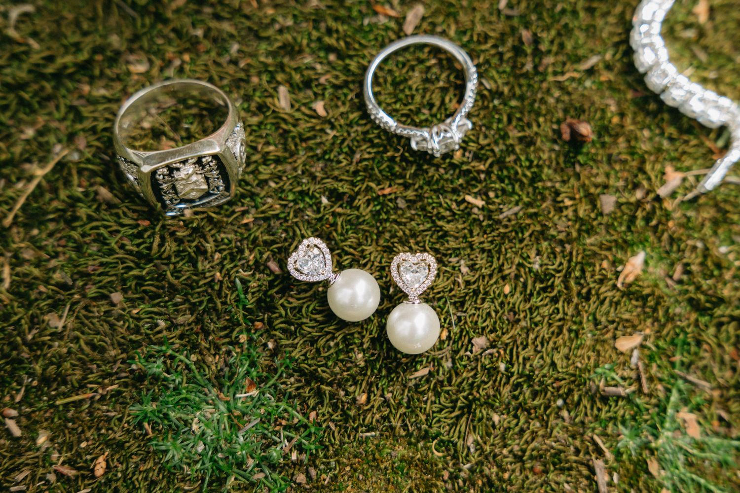 Wedding jewelry and accessories displayed on green grass including rings, pearls and bracelets.