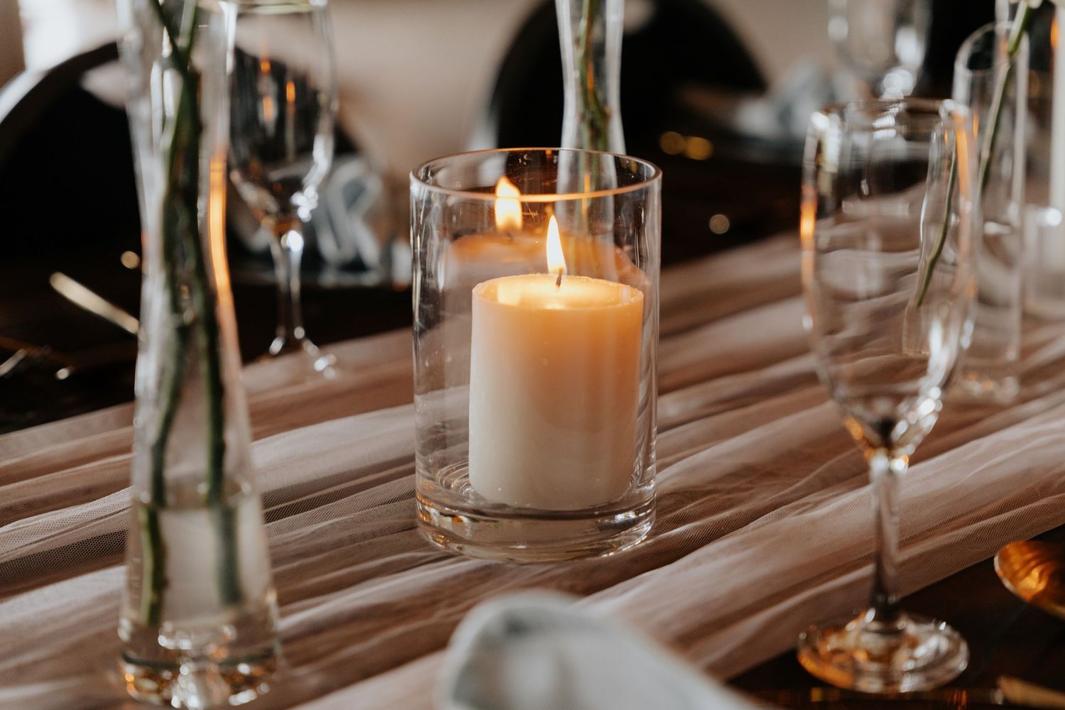 Wedding reception table decorated with elegant candles and simple glass vases.