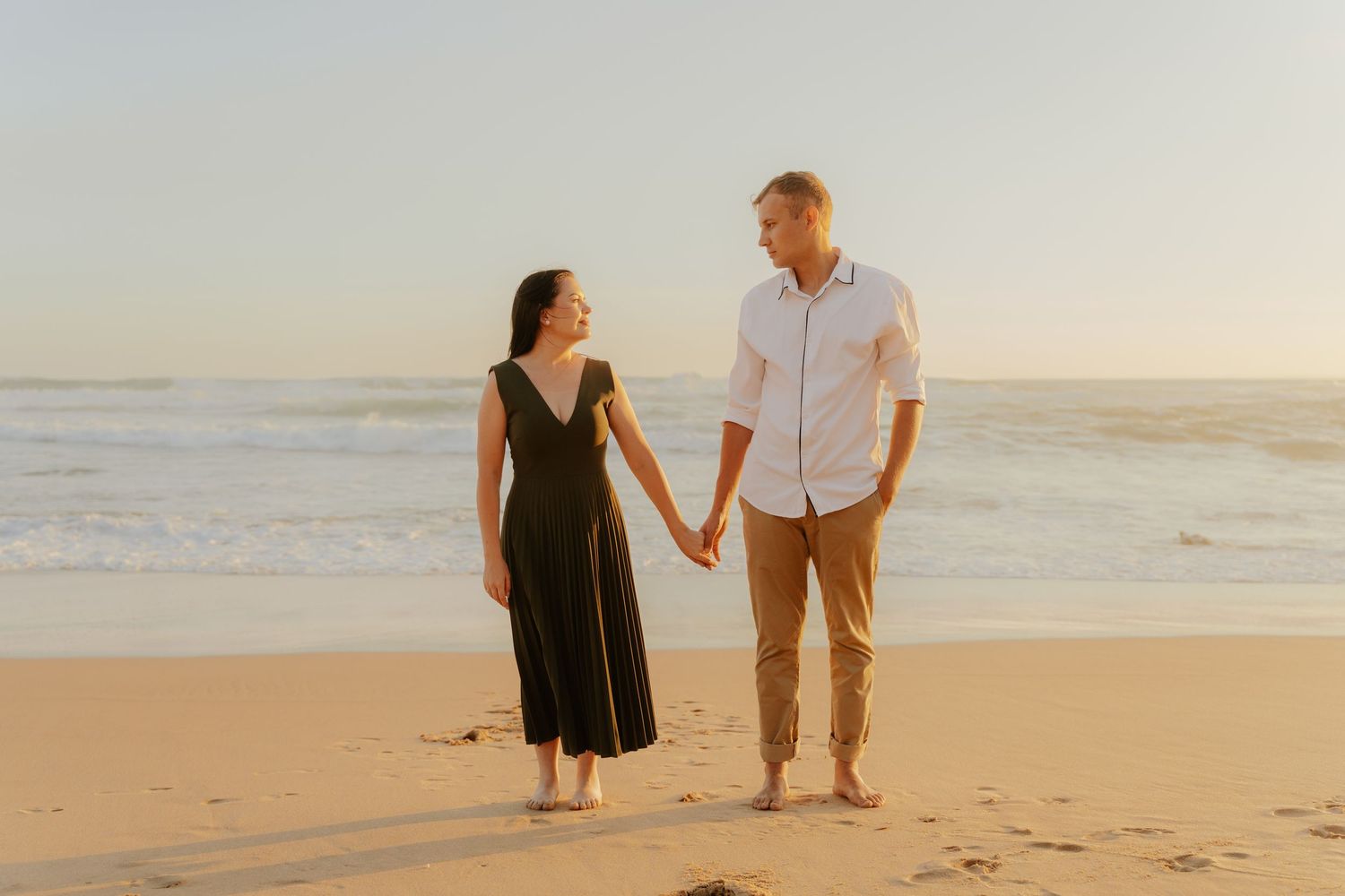 Couple walking hand in hand along a sandy beach at sunset during a romantic seaside stroll.