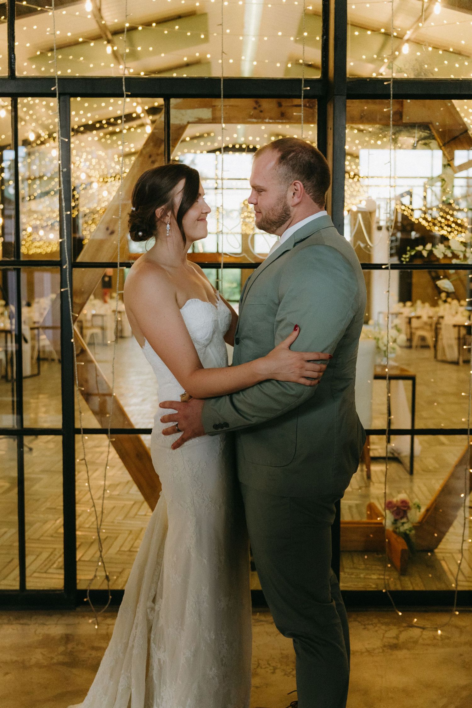 Romantic wedding couple embraces under twinkling lights at their reception venue.