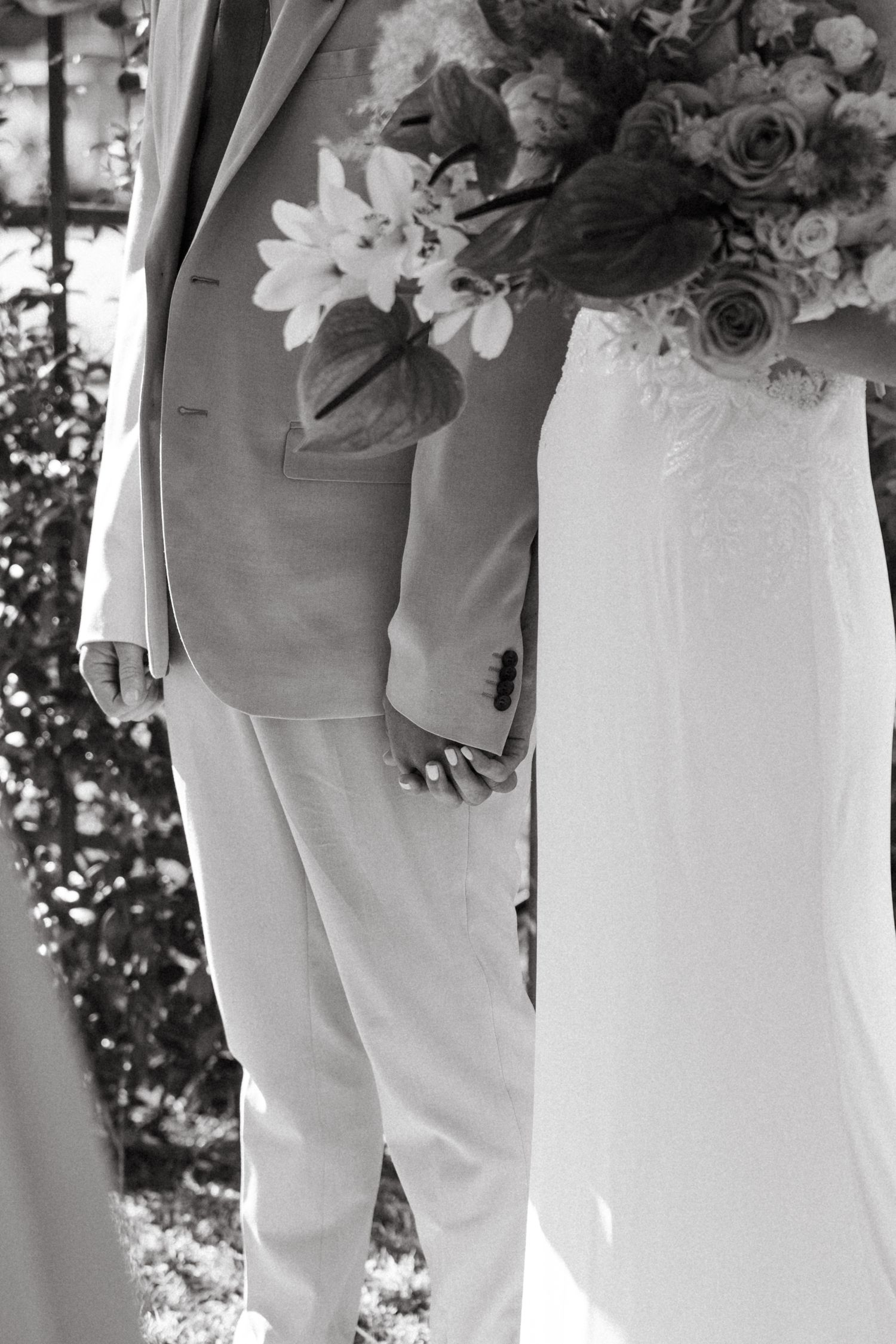 Black and white photo showing wedding party members holding floral bouquets while wearing white attire.
