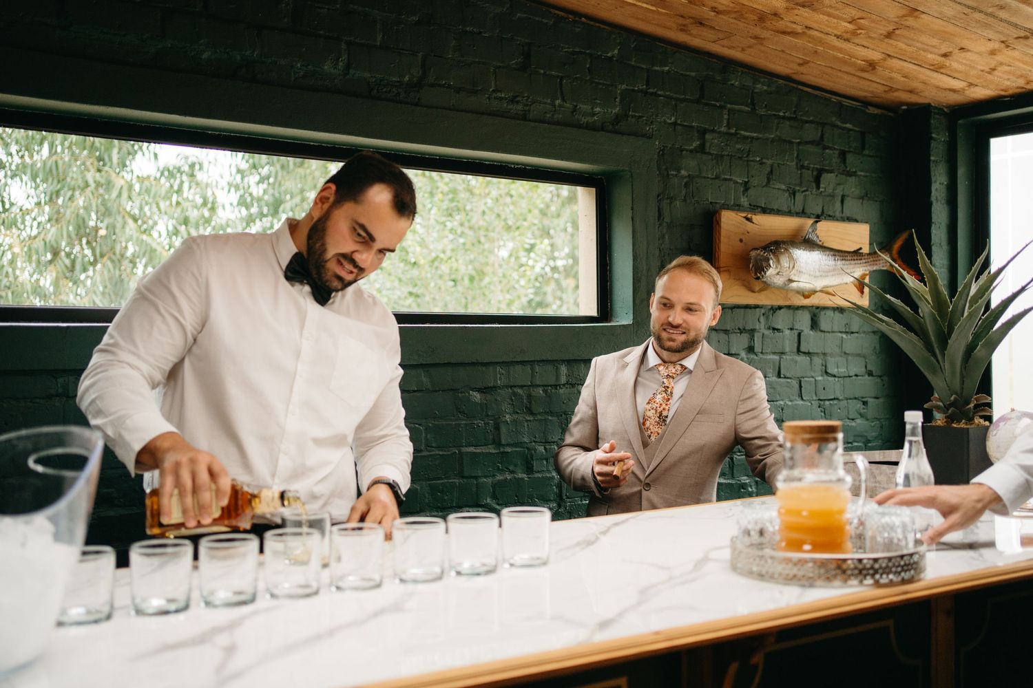 Bartenders preparing drinks at a modern bar counter with wooden details and black brick wall.