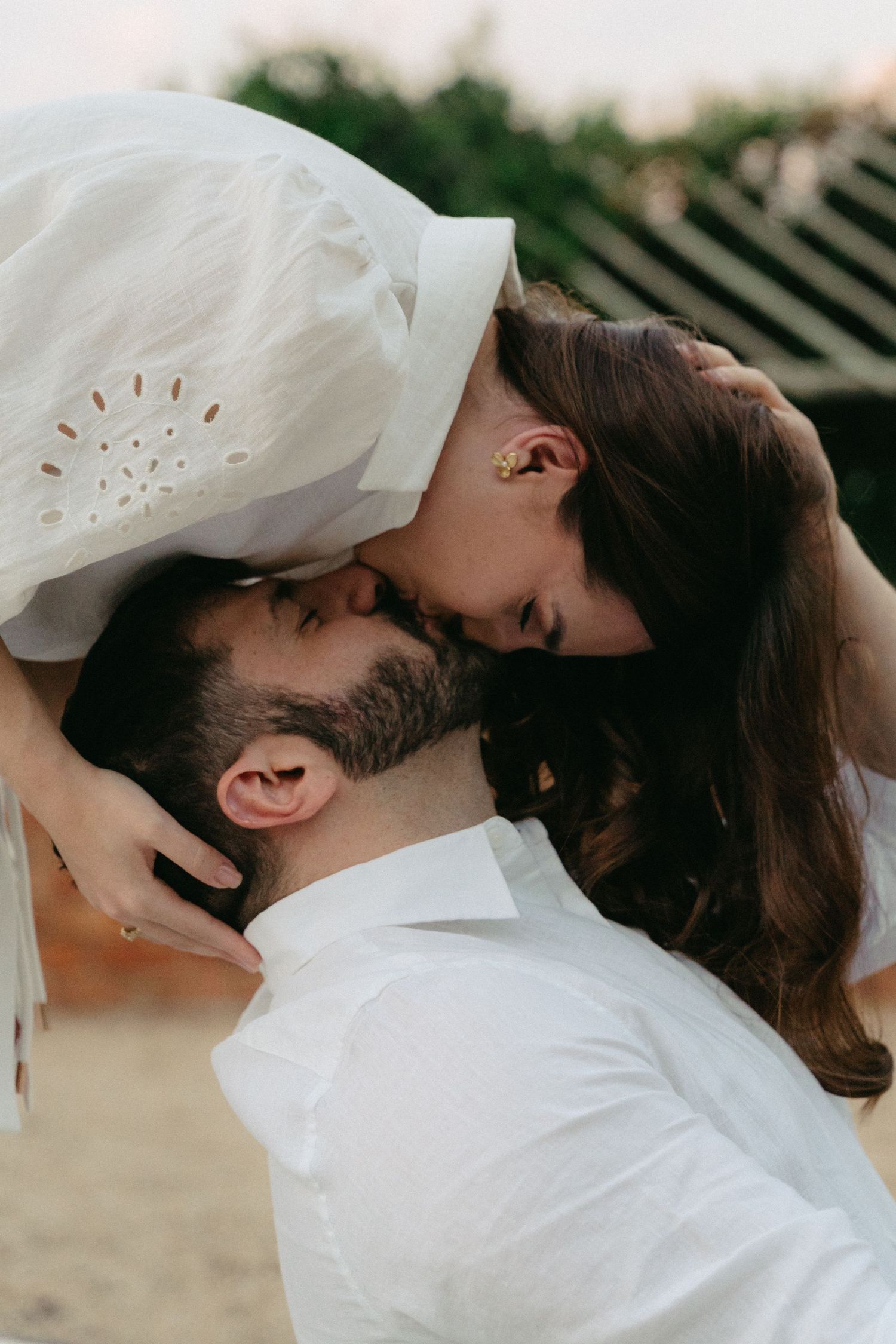 A romantic couple in white clothing share an intimate kiss outdoors in a series of candid photos.