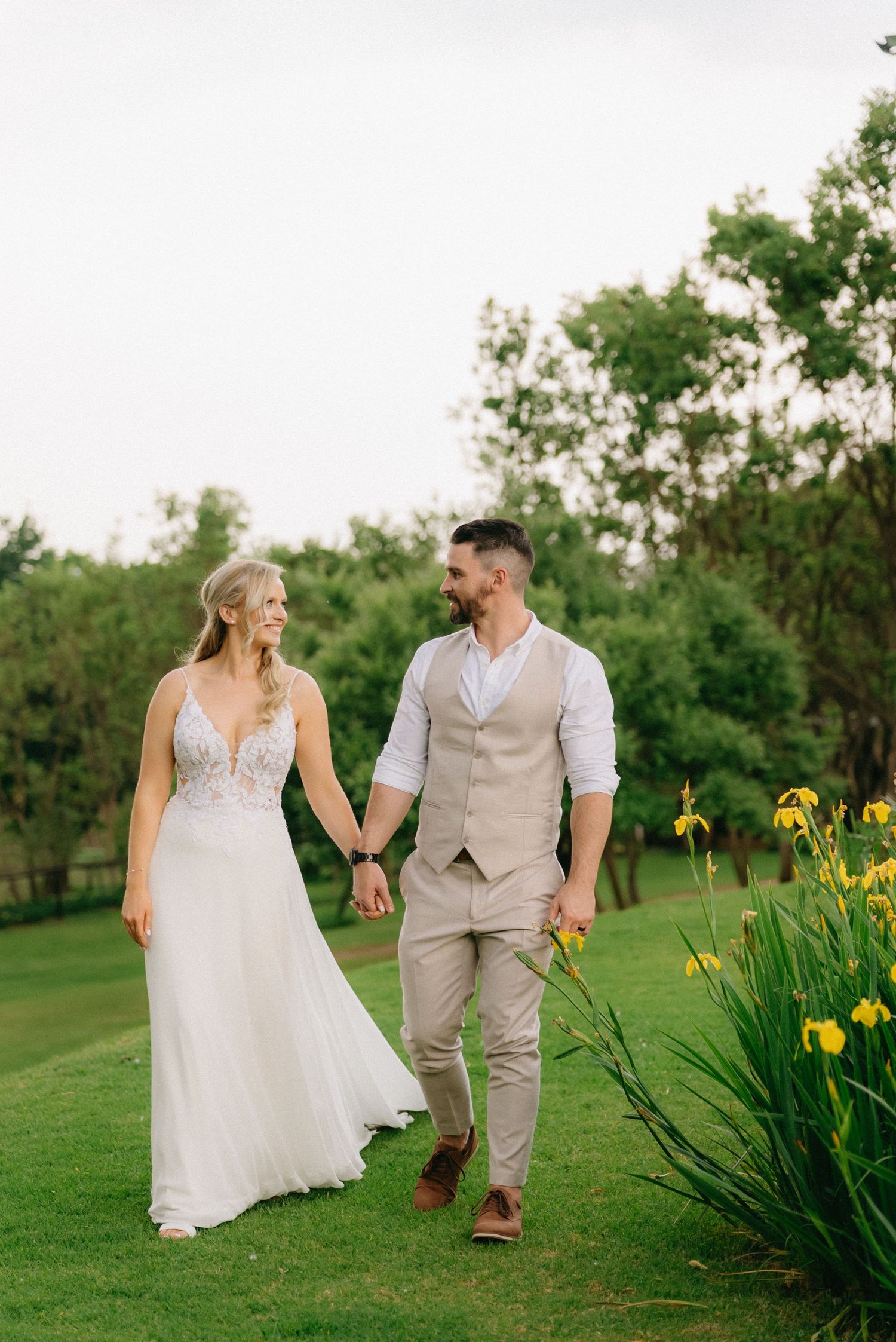 Couple walks through a garden path with blooming yellow irises on a sunny spring day.
