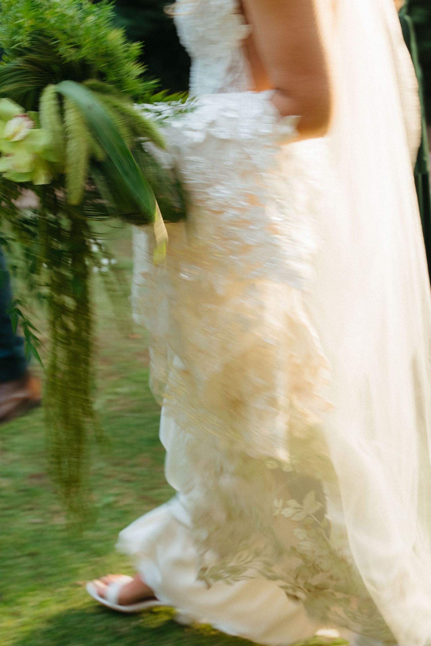 Motion blur shot of bride in ruffled lace wedding gown walking on green grass with floral bouquet at Rosemary Hill in Pretoria