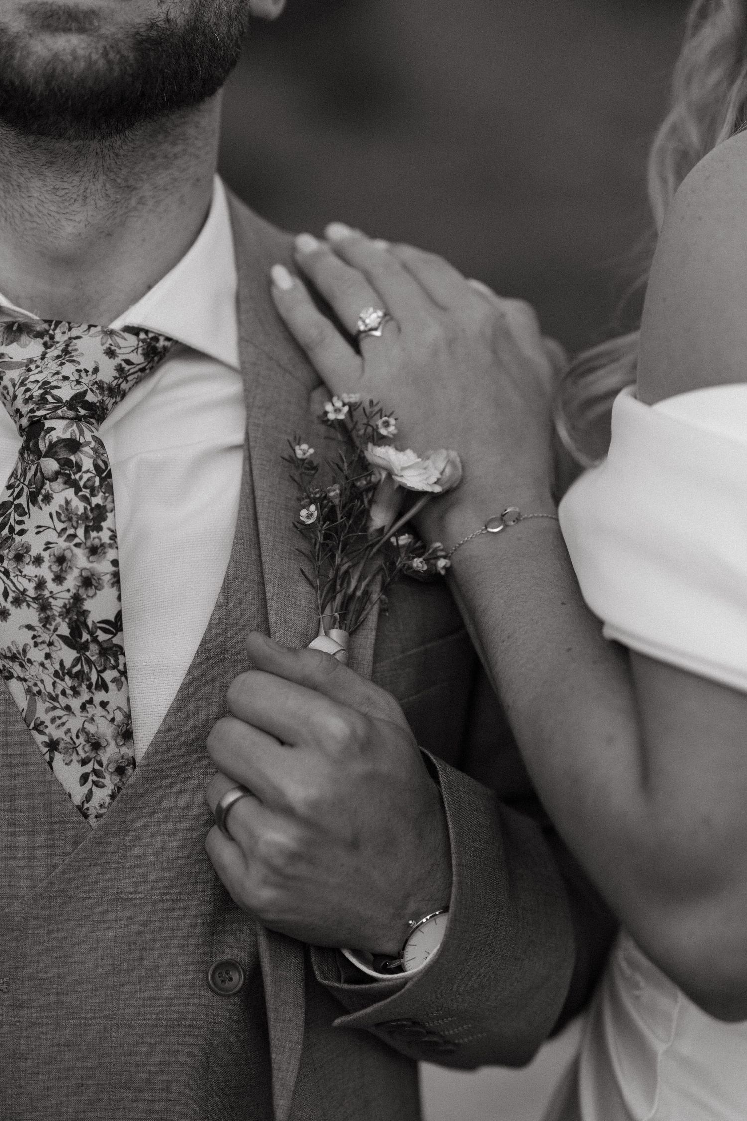 Black and white close-up of hands holding delicate floral details during an intimate wedding moment.