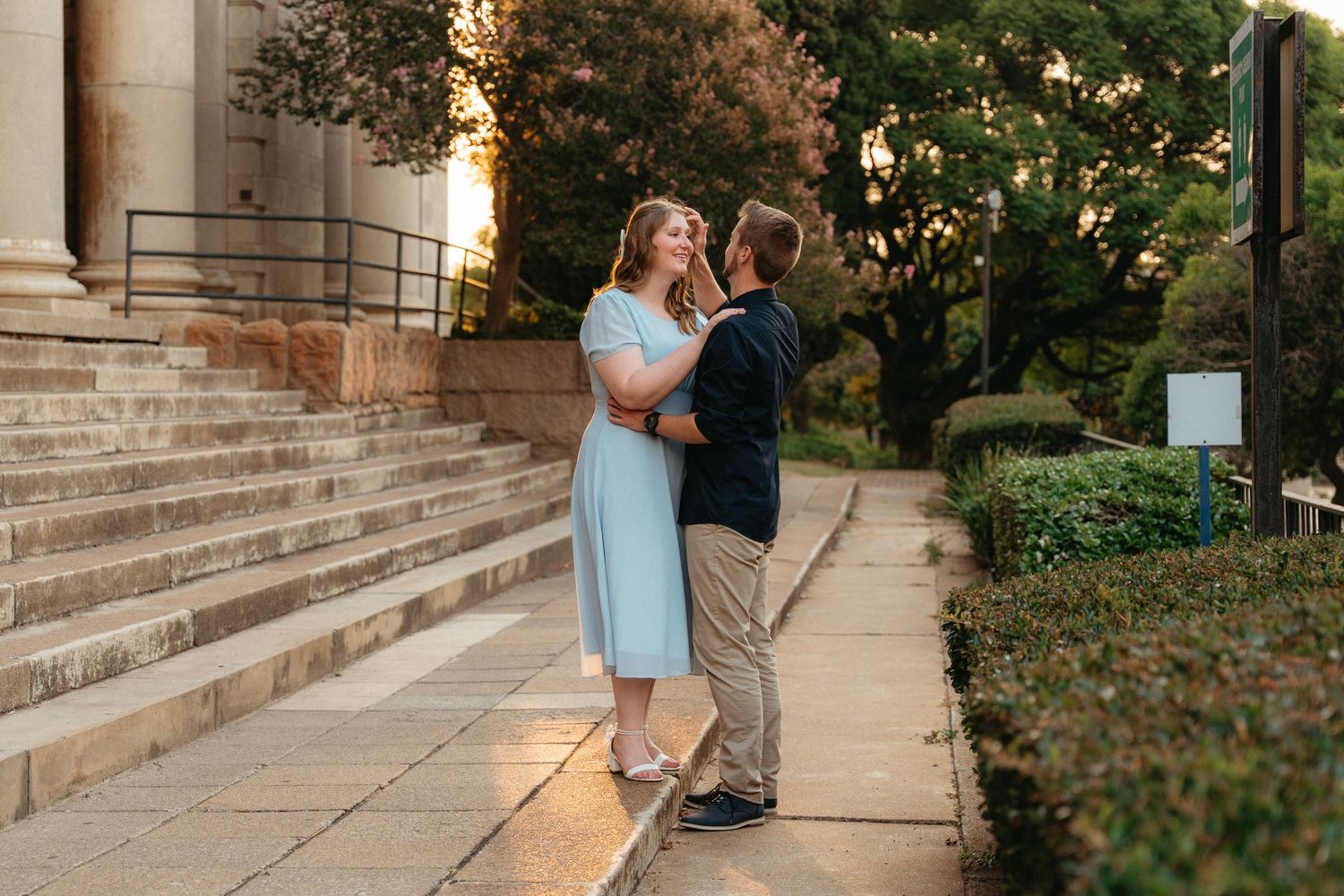 A couple shares a romantic moment on stone steps during golden hour at sunset.