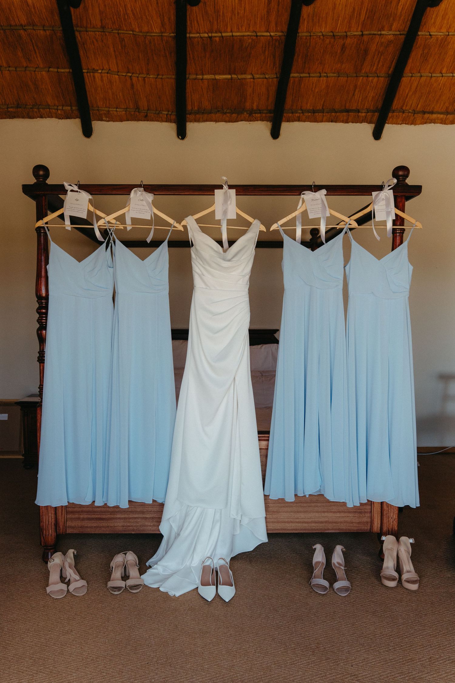 Wedding dresses and light blue bridesmaid dresses hanging on wooden hangers with matching shoes displayed below.