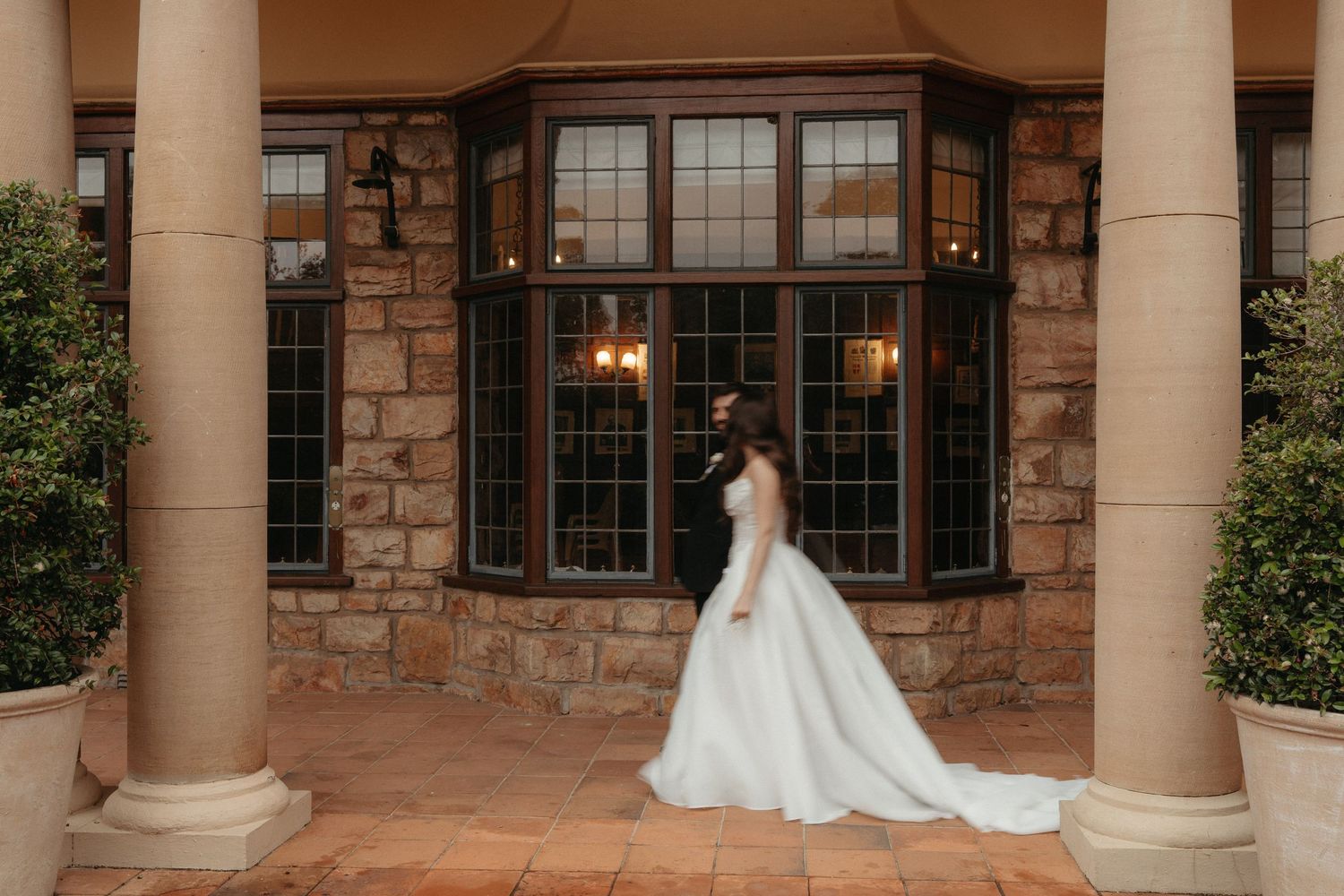 Bride in elegant white ball gown poses between stone columns at historic wedding venue, Glenshiel
