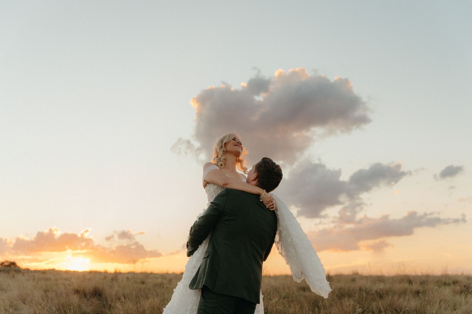 Groom lifting bride in white dress against stunning golden sunset sky in the Free State