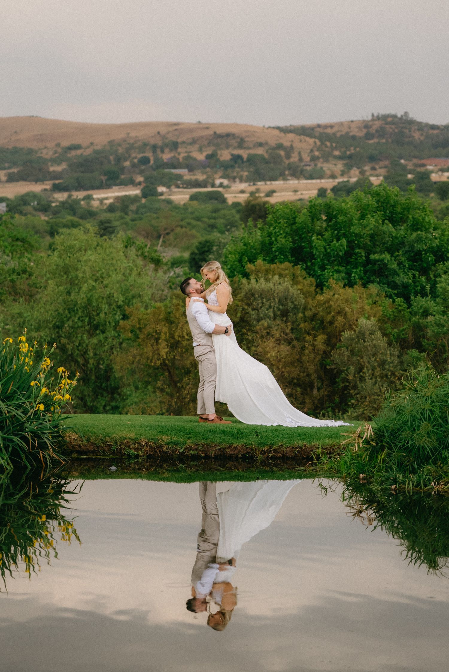 Wedding couple in elegant attire posing against a scenic mountain landscape.