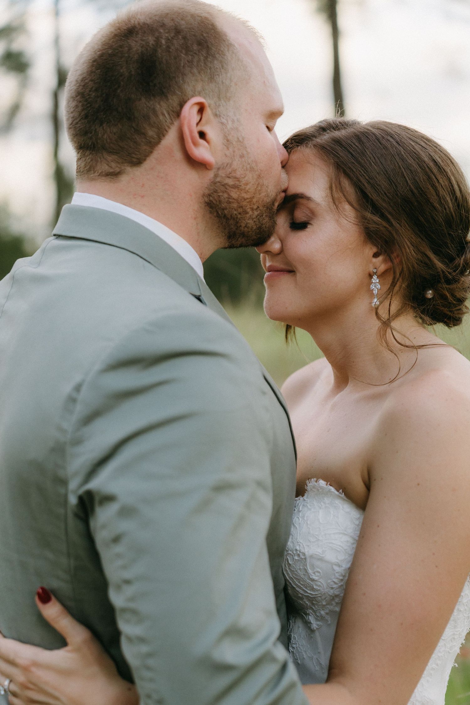 A romantic moment between newlyweds as they embrace, with the bride in a white lace gown and groom in a gray suit.