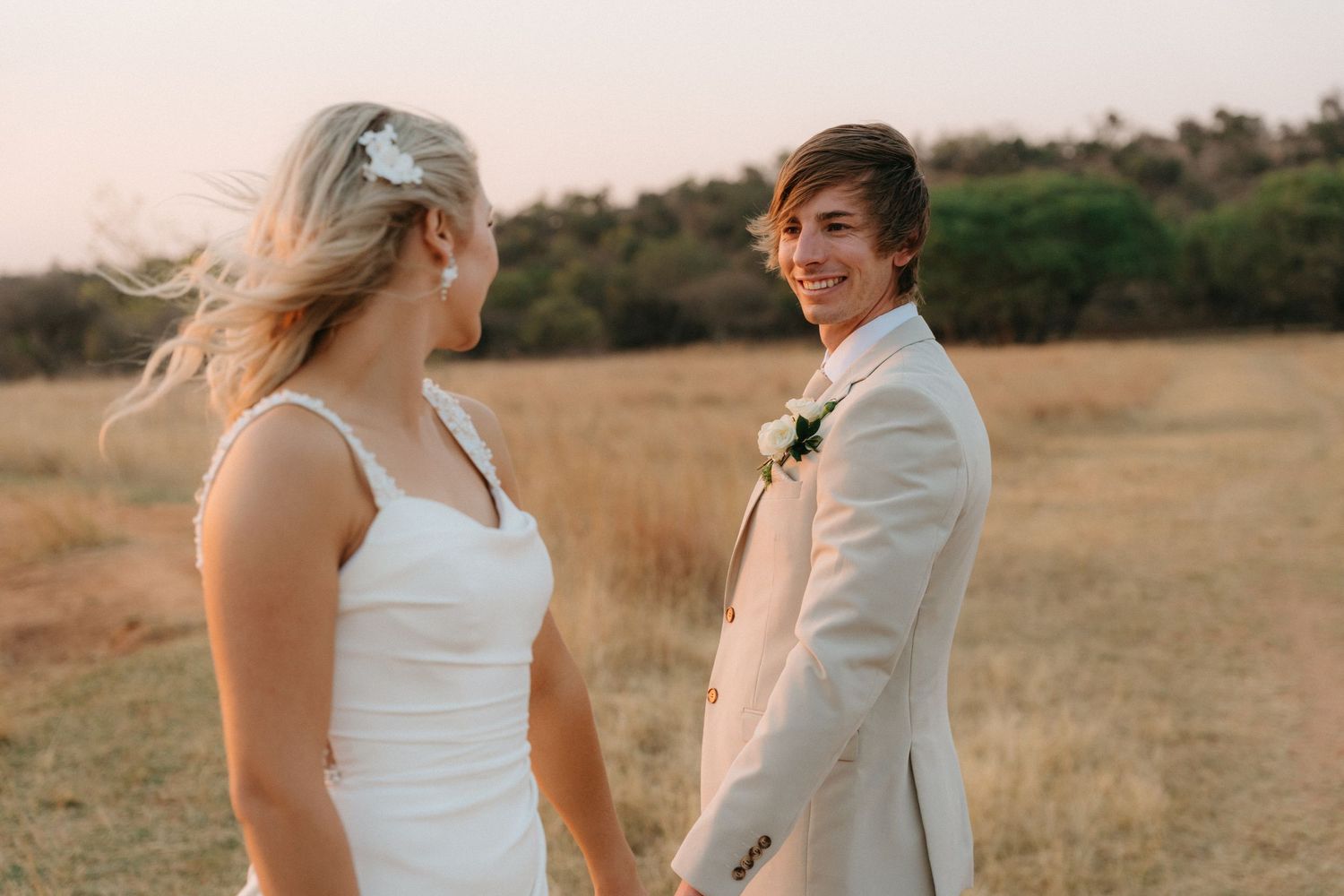 Wedding couple sharing a candid moment in a golden field at sunset.