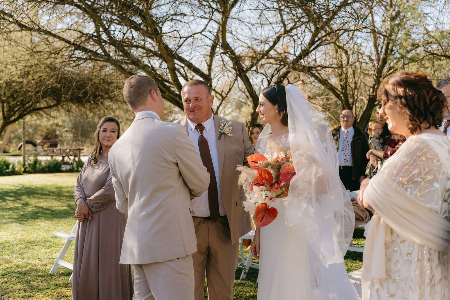 An outdoor wedding ceremony under trees with guests gathered to witness the exchange of vows.