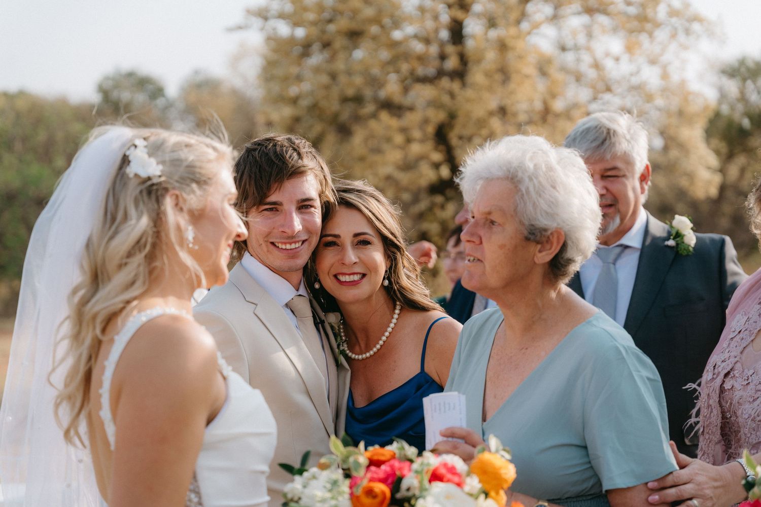 Wedding party and family members sharing emotional moments during outdoor celebration.